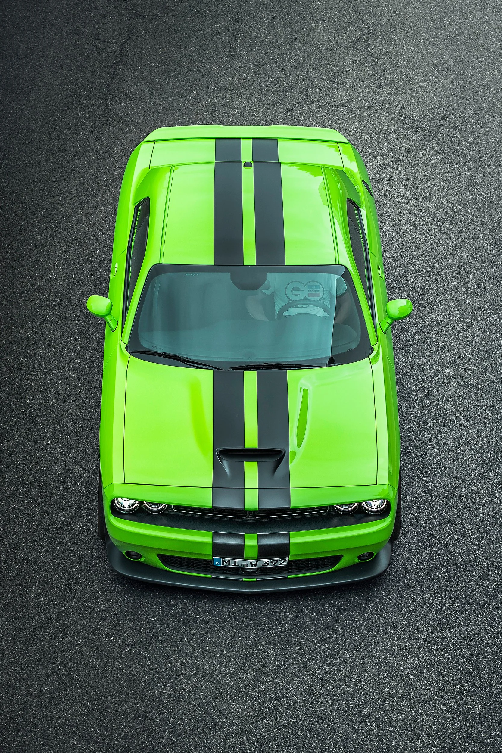 Obere Ansicht eines grünen Muscle Cars mit schwarzen Rennstreifen auf Asphalt.