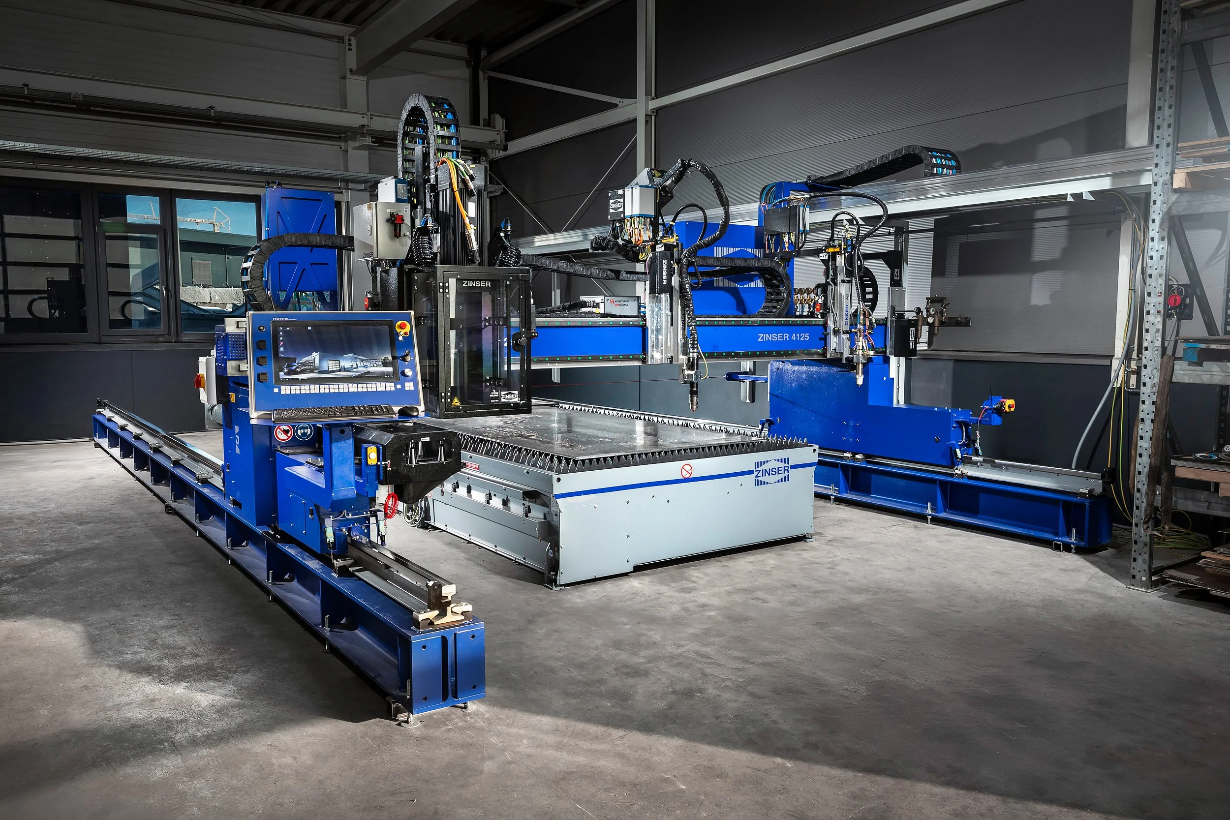 Ein industrieller Roboterschweißautomat in einer Werkshalle, bestehend aus mehreren blauen und schwarzen Komponenten, mit einem Computerterminal für Steuerung und Überwachung.