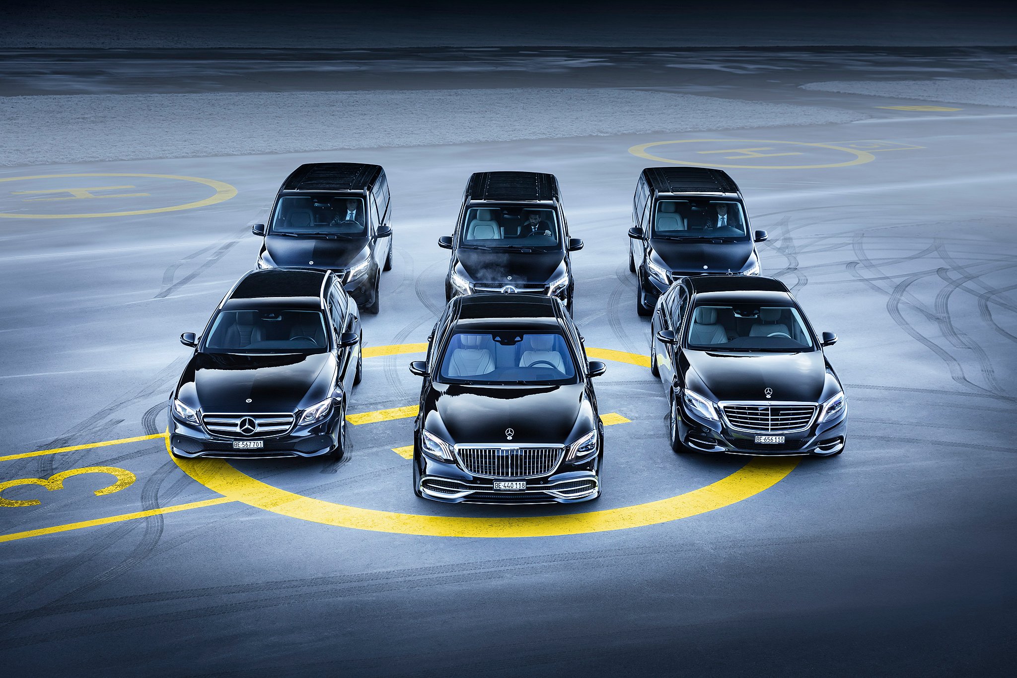 Sechs schwarze Mercedes-Benz Fahrzeuge sind in einem Kreis auf einem flachen Platz geparkt. Jeder Wagen ist auf einem markierten Parkplatz, die Reifen sind Spuren auf dem Boden hinterlassen.
