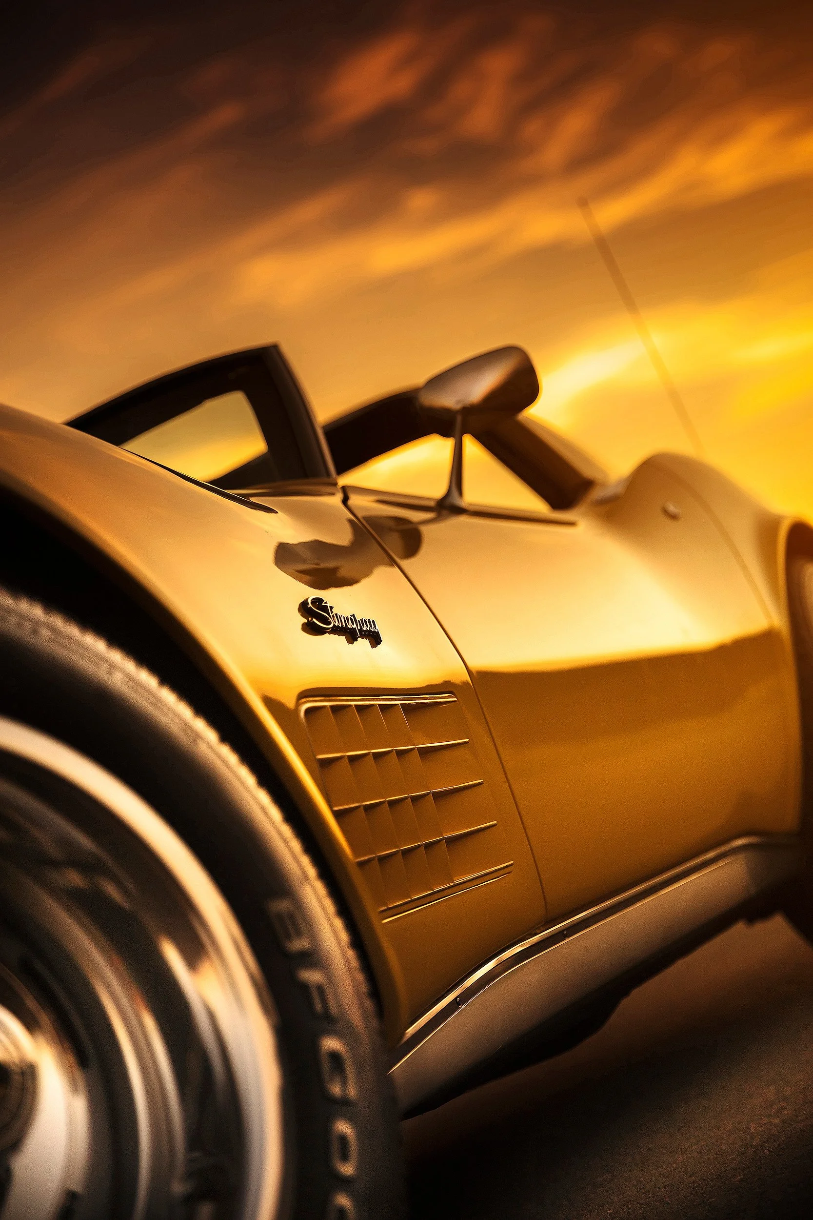 Nahaufnahme einer schwarzen Ferrari-Auto mit Sonnenuntergang im Hintergrund, Fokus auf das vordere Rad und das Logo auf der Seite.