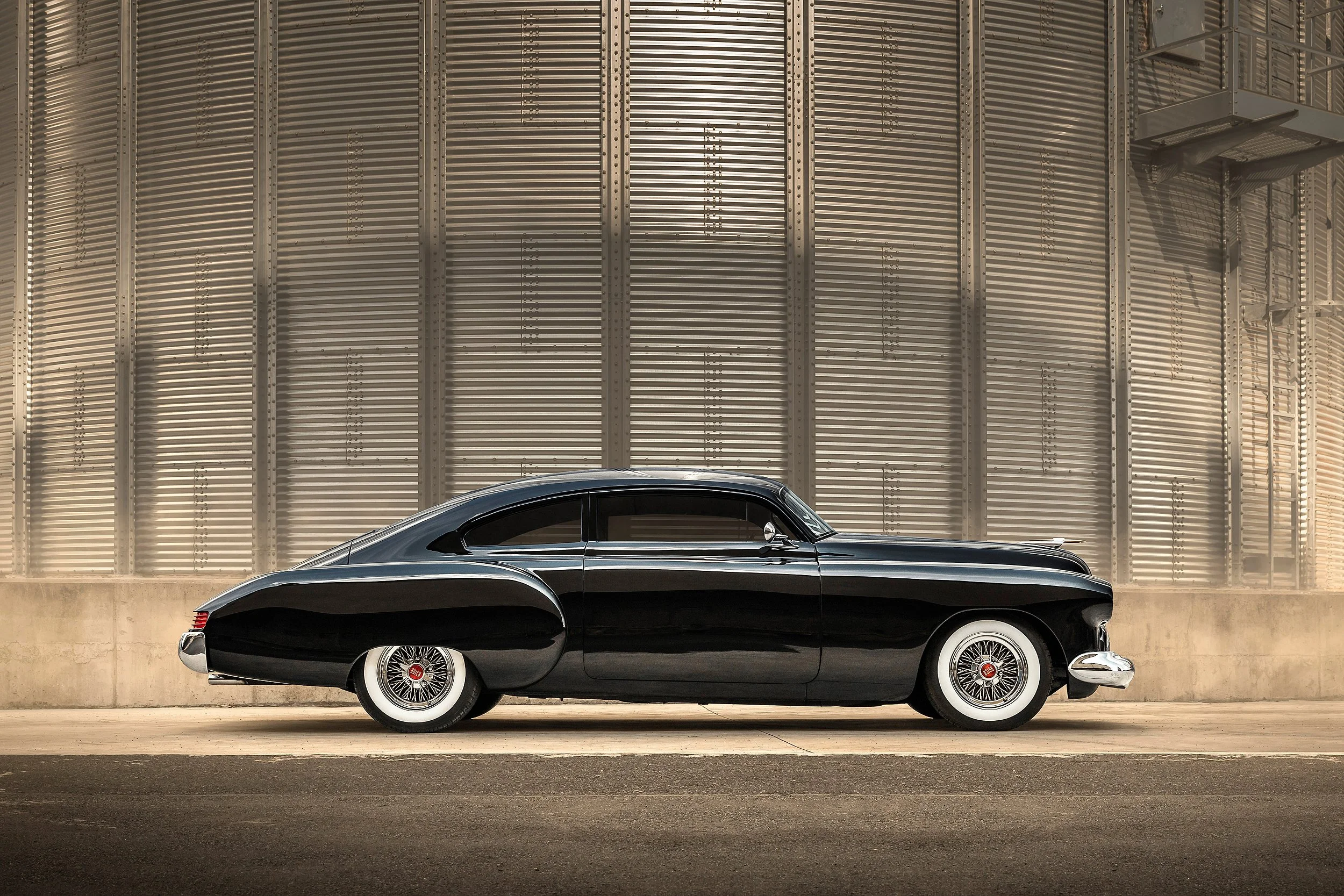 Ein schwarzer Oldtimer-Auto vor einer großen metallic Säulenwand.
