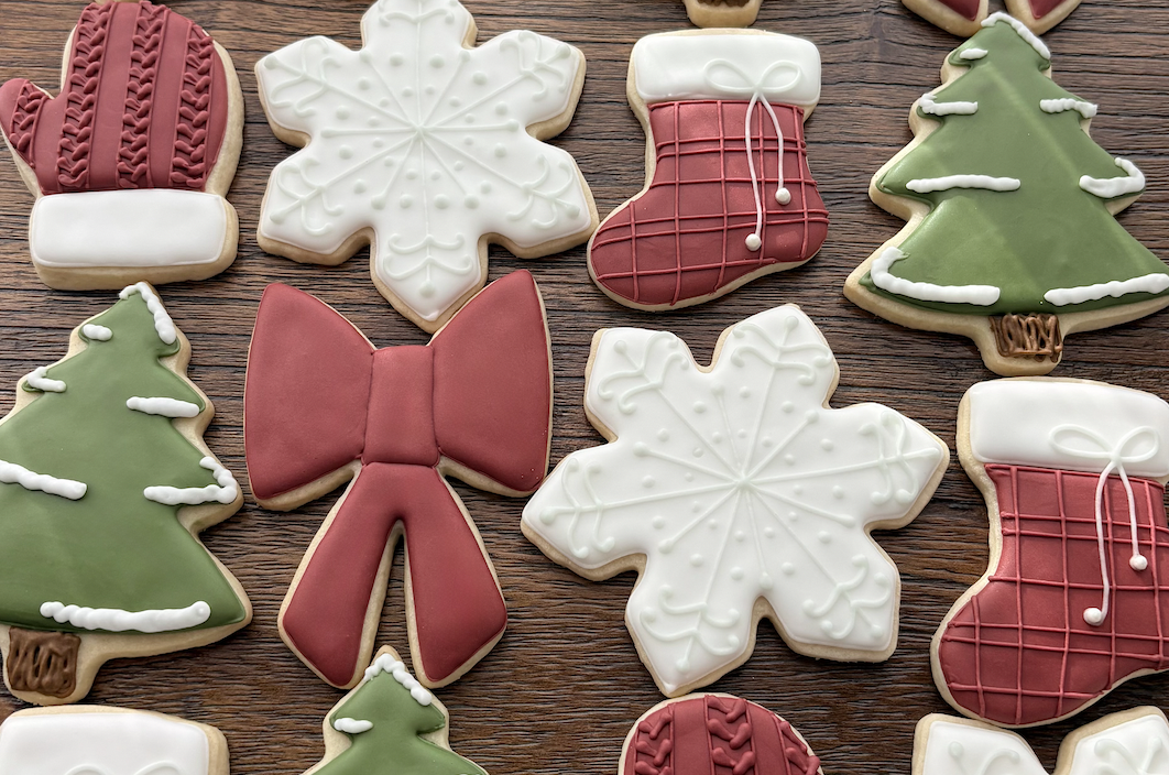 Decorated Christmas cookies shaped like snowflakes, Christmas trees, stockings, a bow, and a mitten, all laid on a wooden surface.