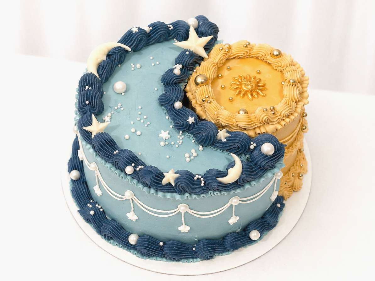 A decorated cake with a moon and stars theme, featuring blue and yellow frosting, gold and white accents, and celestial decorations.