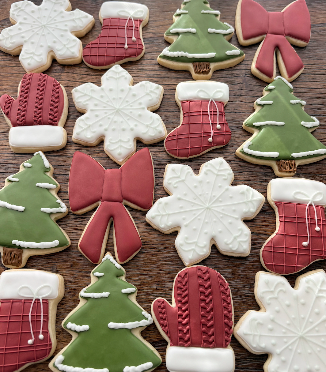 Assorted Christmas holiday cookies shaped like snowflakes, Christmas trees, mittens, bows, and stockings decorated with icing on a wooden surface.