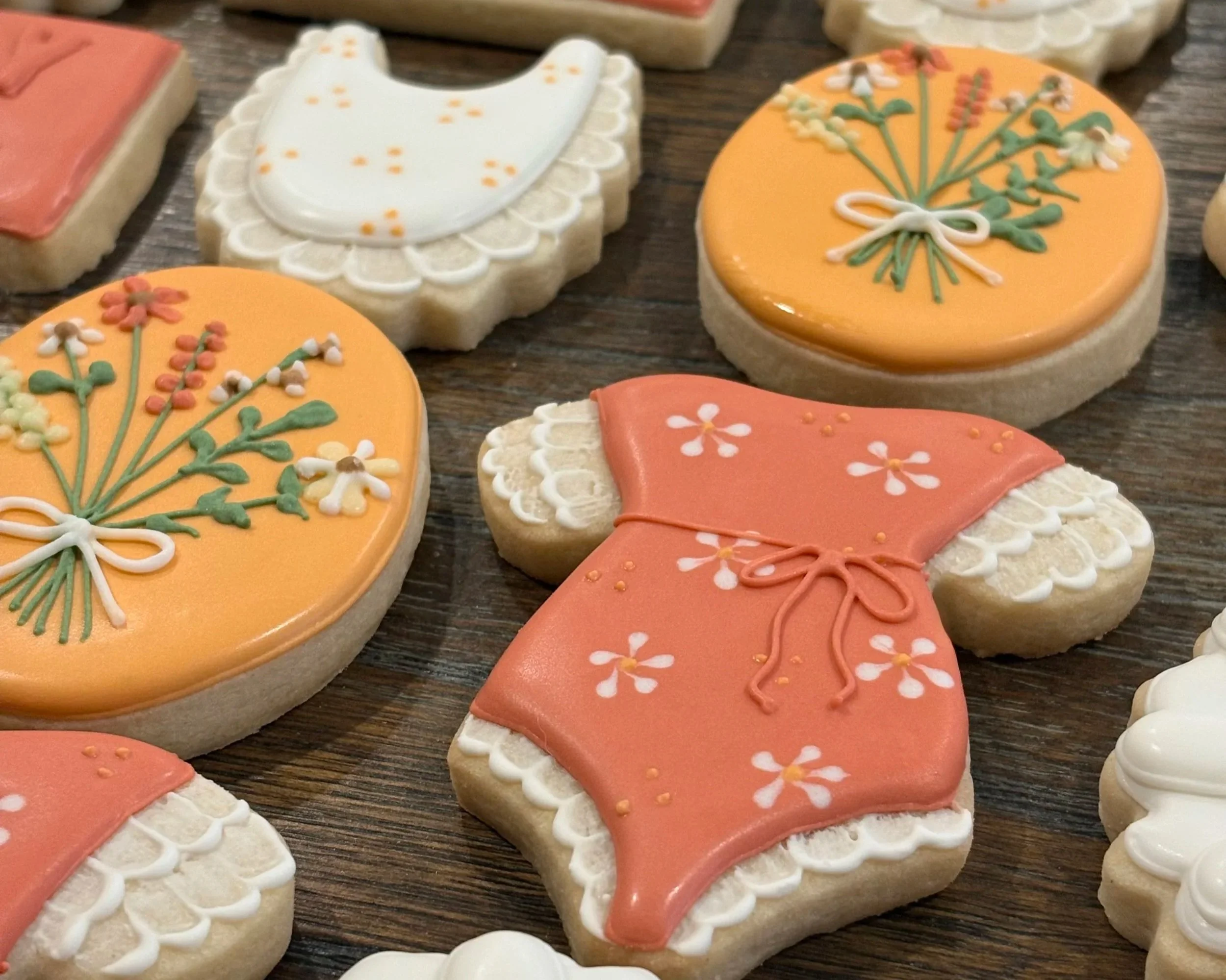 Decorated frosted cookies with floral and clothing patterns on a wooden surface.
