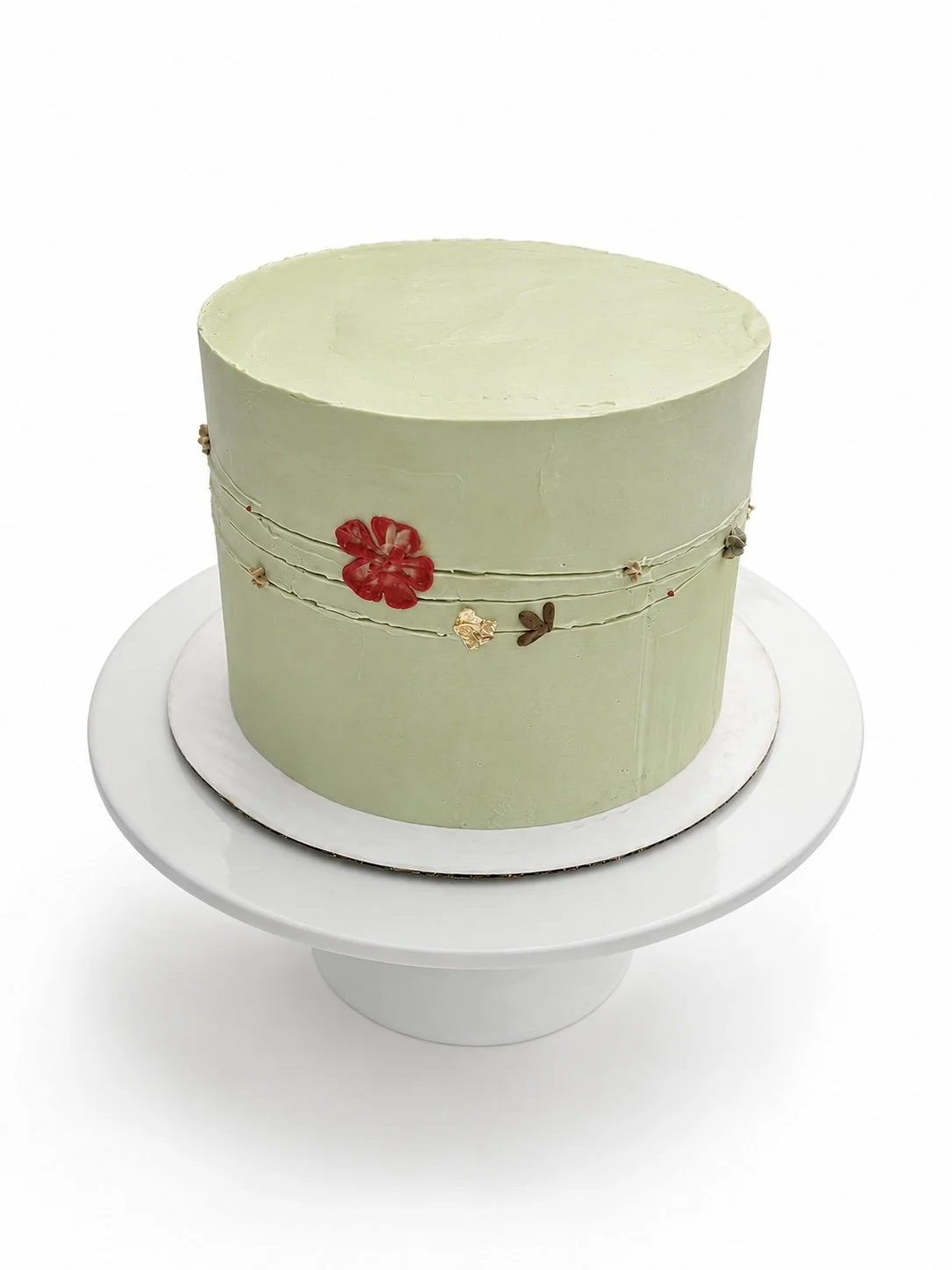 A light green round cake with a smooth surface, decorated with small, colorful flower and leaf designs along a horizontal line, placed on a white cake stand.