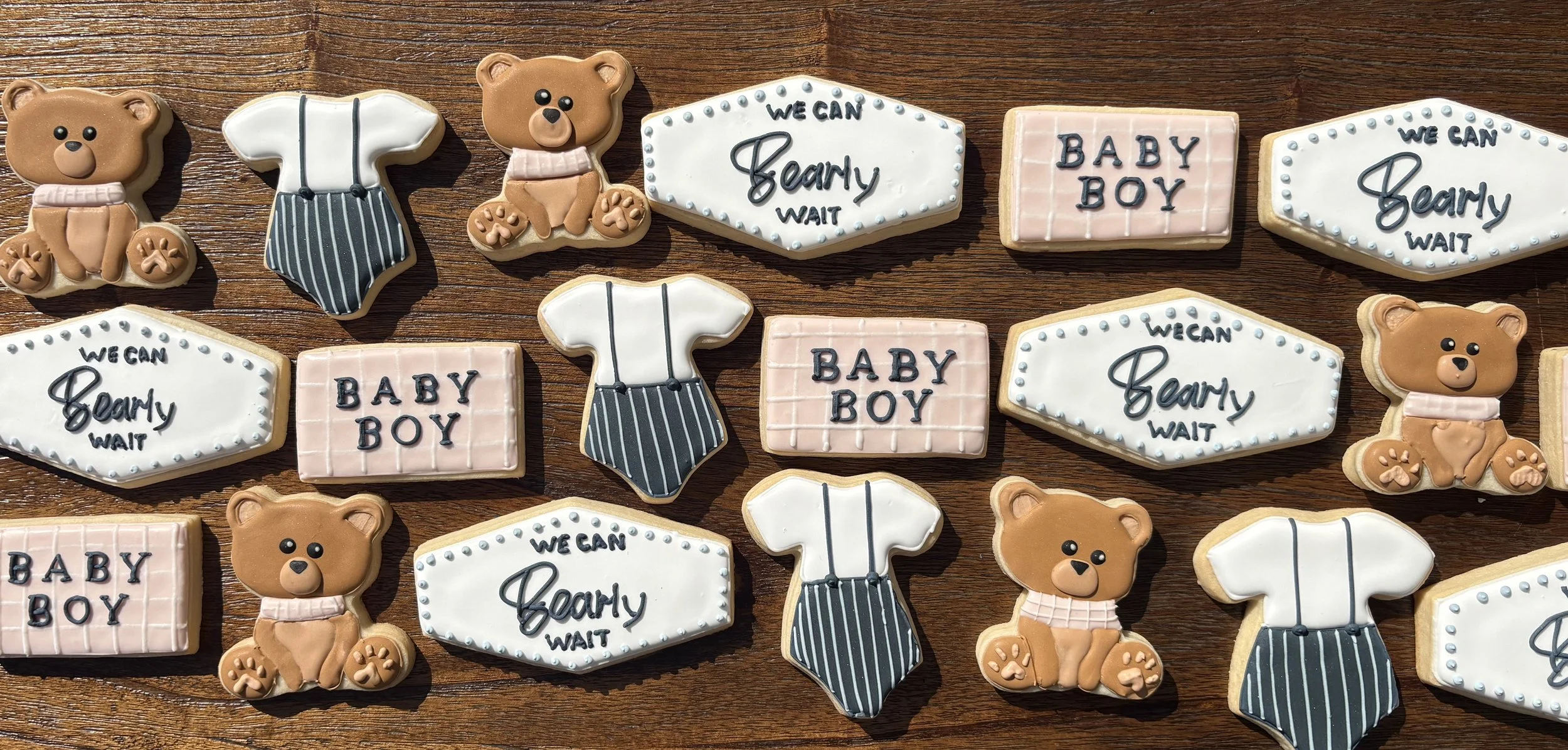 Assorted cookies decorated with bear, baby boy, and tie designs, arranged on a wooden surface.