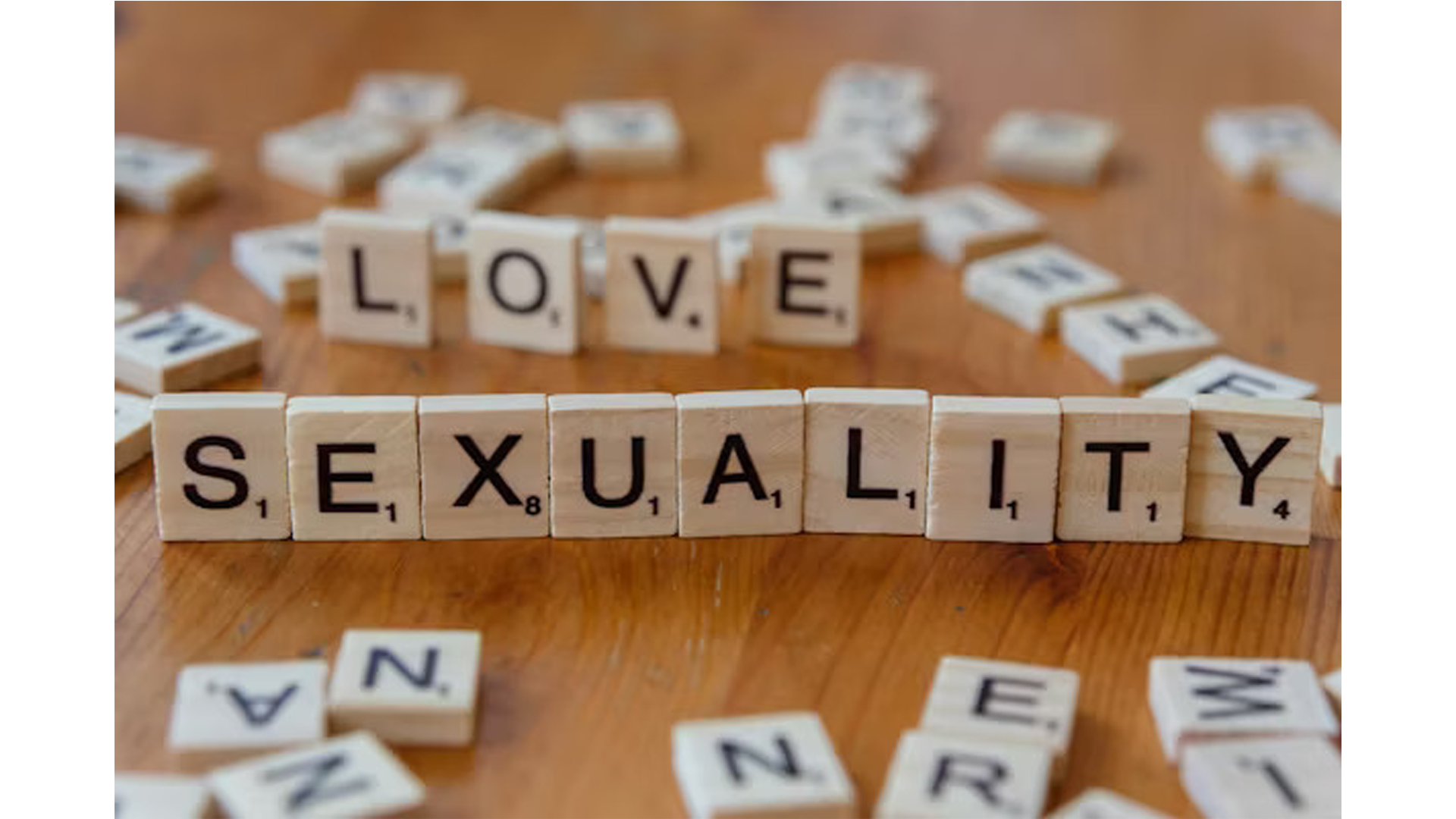 Scrabble tiles spelling out 'LOVE' and 'SEXUALITY' on a wooden table with scattered tiles around them.