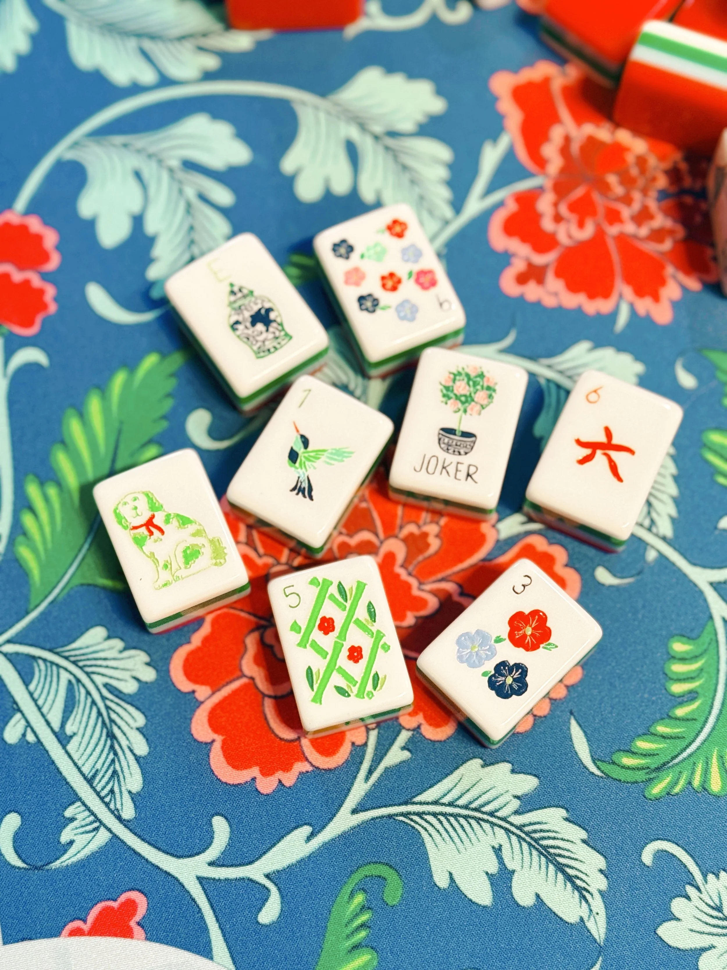 Assorted decorative domino tiles with floral and animal illustrations, arranged on a colorful floral tablecloth.