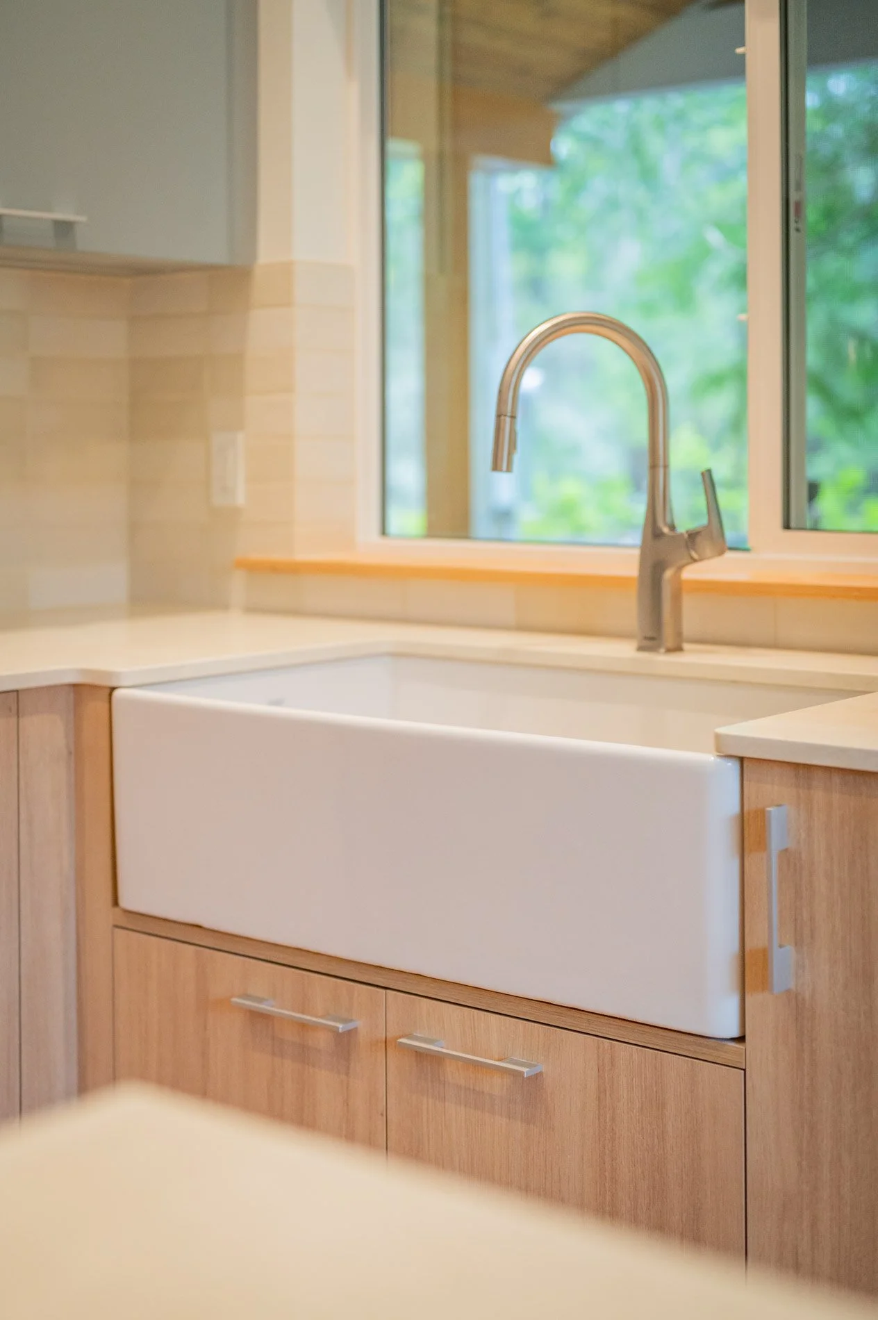 A farmhouse kitchen sink beneath a window with a view of a green outdoor scene.