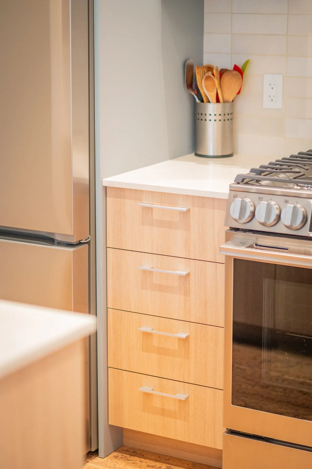 Countertop with a silver utensil holder containing wooden spoons and spatulas next to a stove in a modern kitchen.