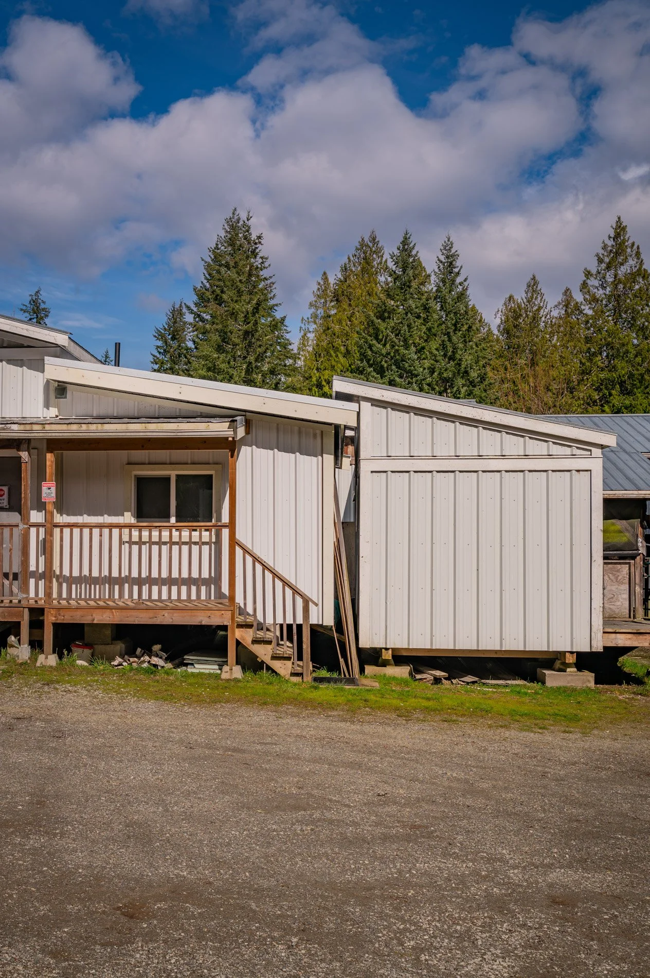 A white building with a small porch and stairs, surrounded by green trees and a blue sky with clouds.