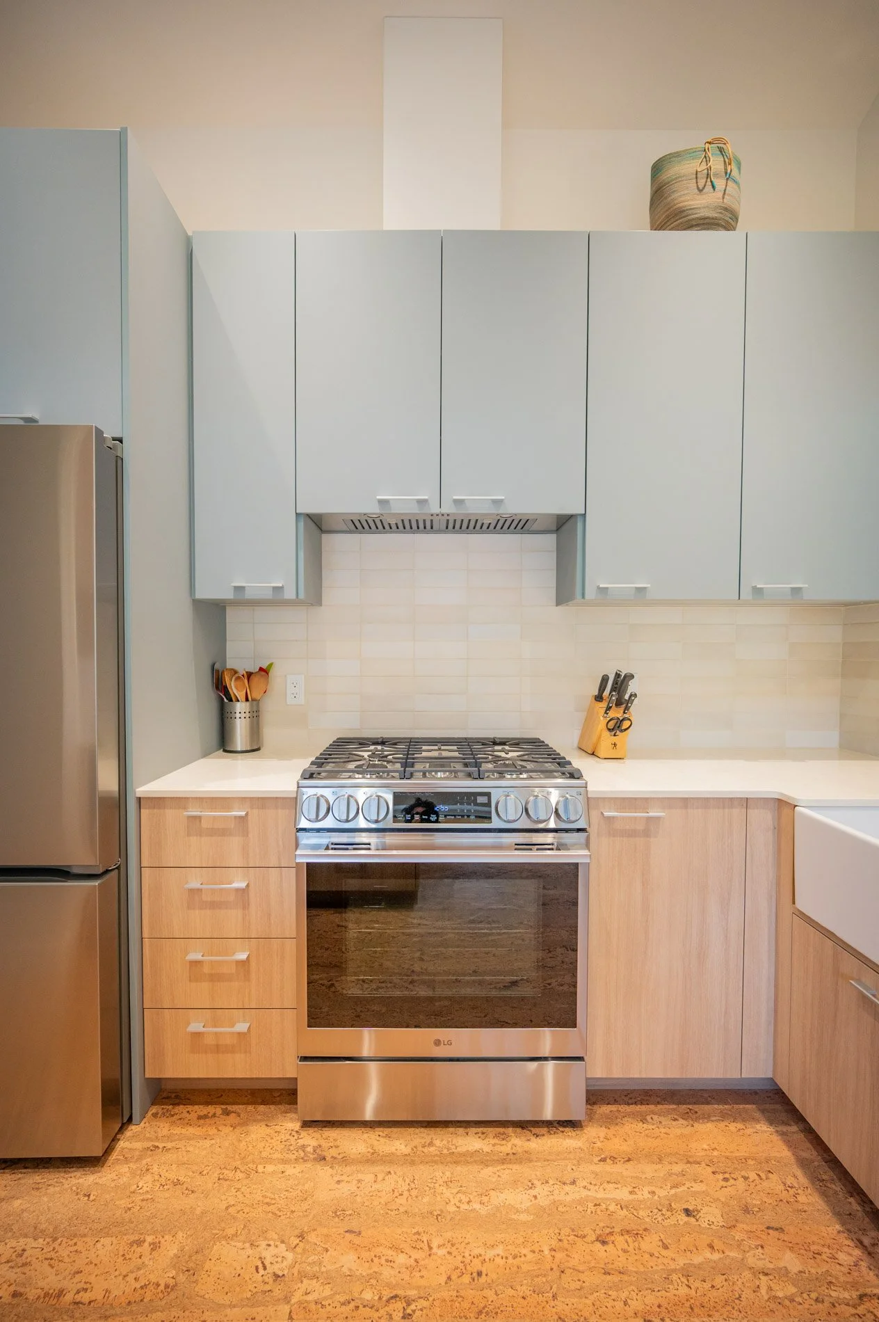 Modern kitchen with a stainless steel LG oven, wooden cabinets, light blue upper cabinets, a white countertop, a utensil holder, a knife block, and decorative pottery on top.