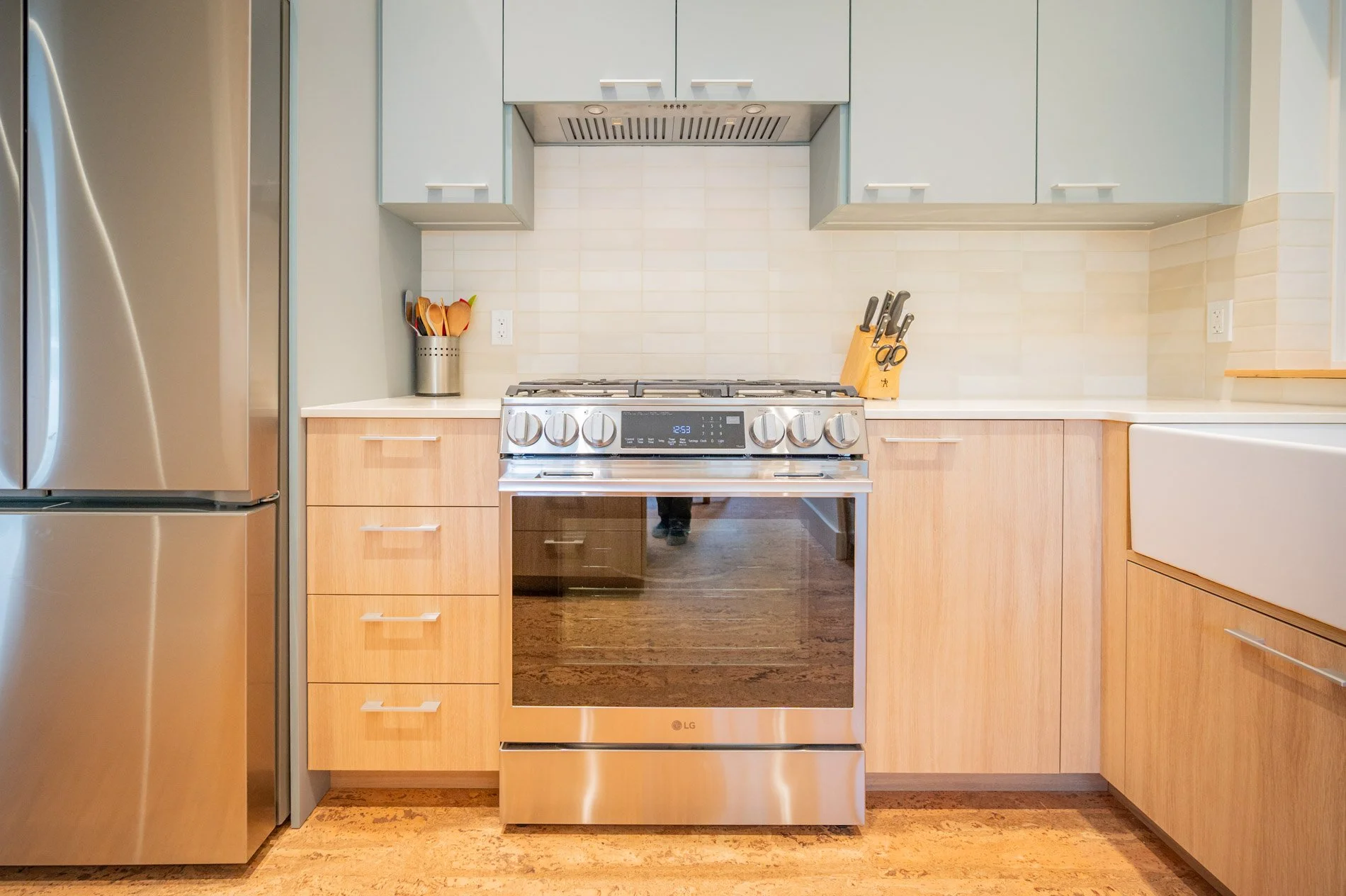 Kitchen with LG stainless steel stove, wooden cabinets, light beige backsplash, and a refrigerator. Countertop with utensils and a knife block.