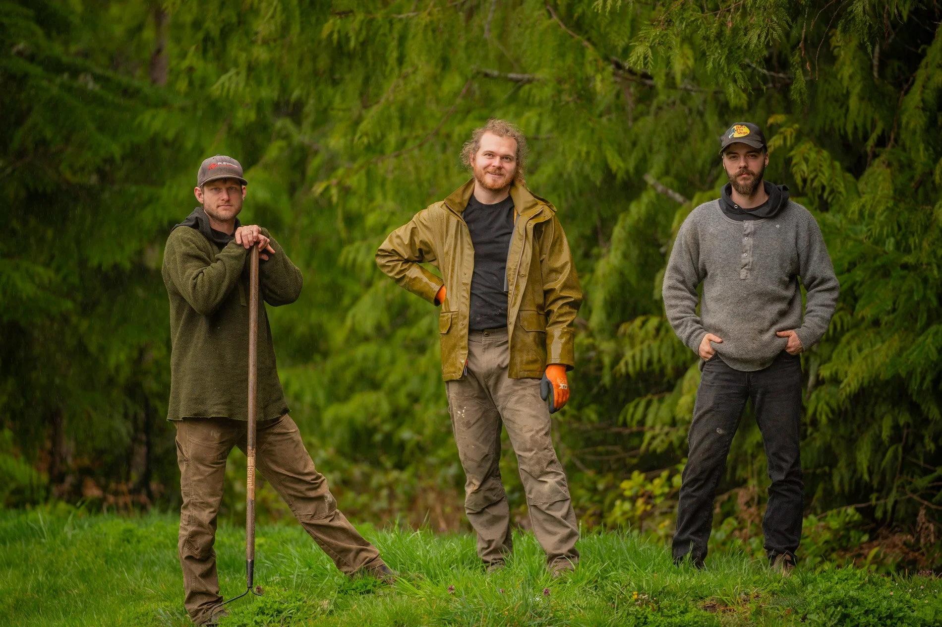 Three men standing outdoors on a grassy area in front of a background of green trees.