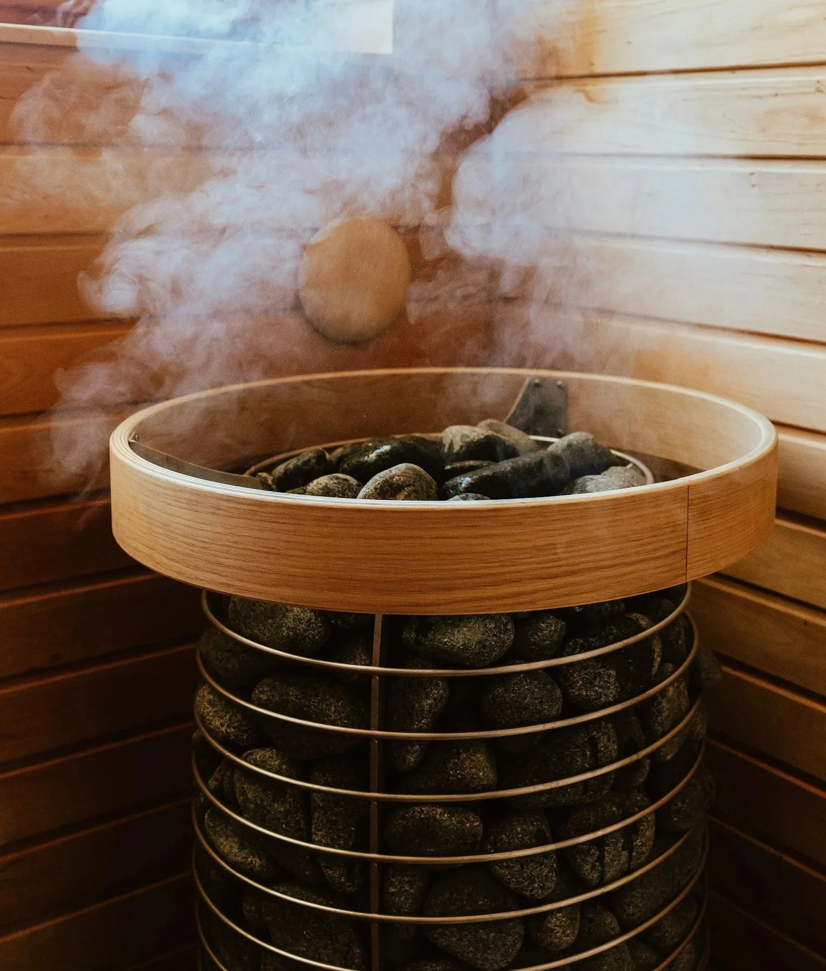 Indoor sauna with wooden walls and a heated rocks heater, emitting steam.