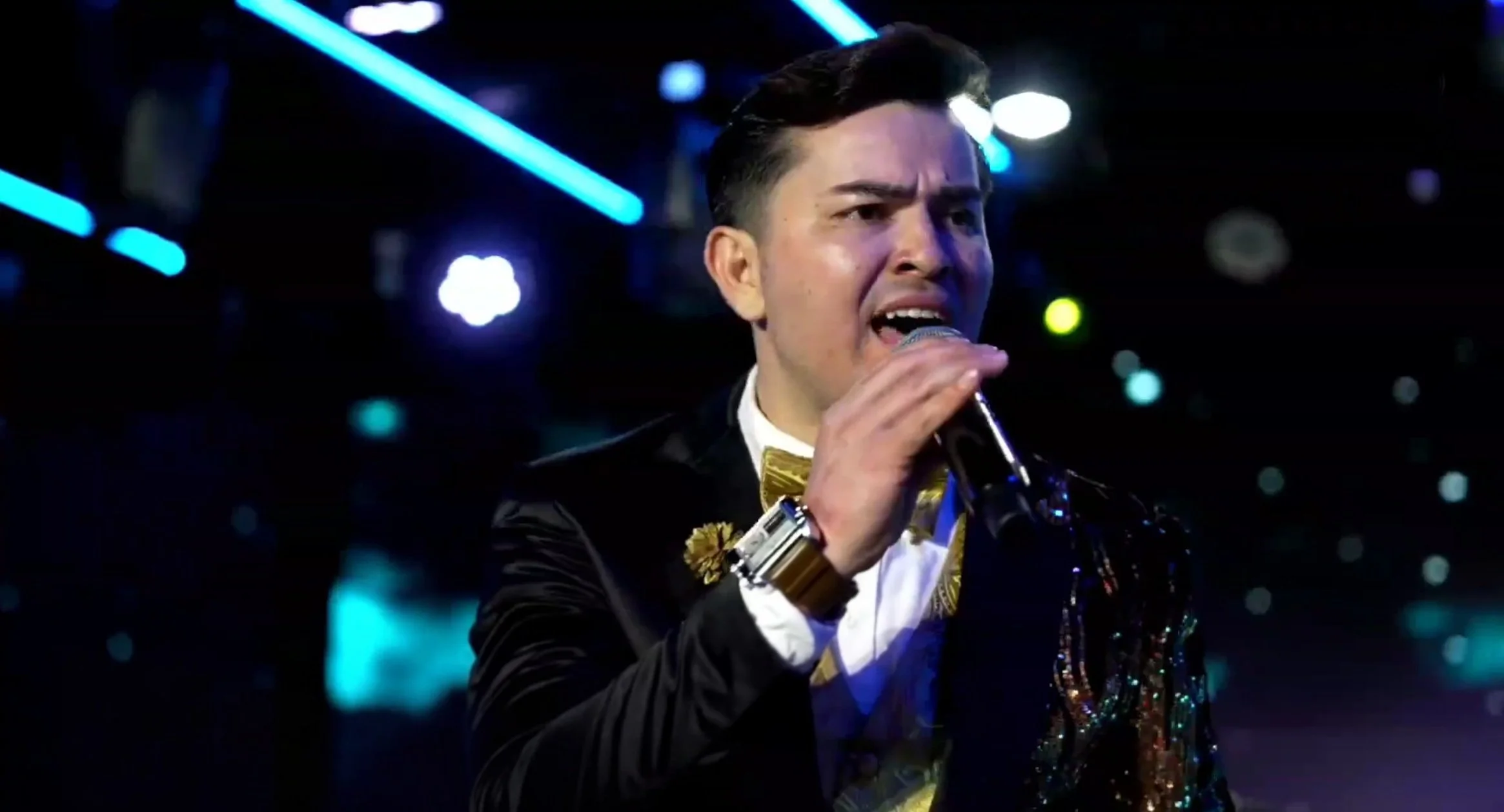 Person singing into a microphone at a nightclub or concert, with colorful stage lights in the background. La voz Guacalito, Alberto Jimenez cantante latino