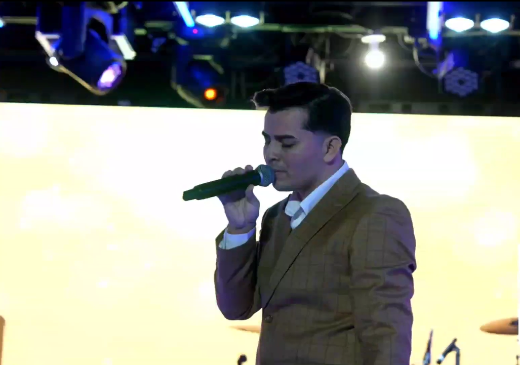 A man in a brown suit singing into a microphone on stage with colorful lighting.El Guacalito, La Voz el Guacalito