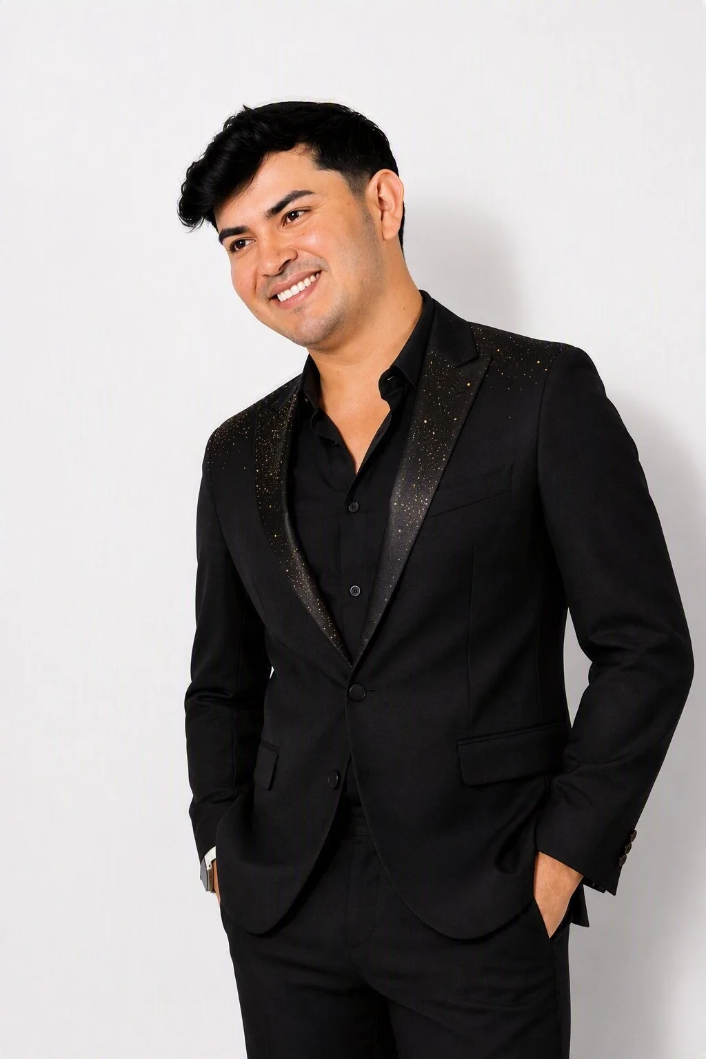 A man wearing a black suit with sparkles on the lapel, black shirt, and a watch, smiling and posing against a plain white background. Alberto Jimenez, Alberto Jimenez Nicaragua, Alberto Jimenez Musica, Alberto Jimenez Veneno