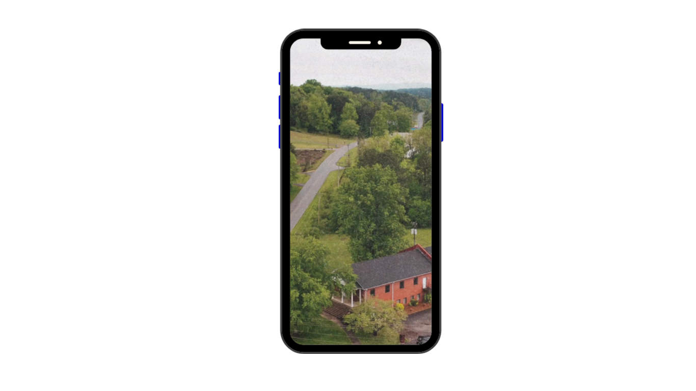 A smartphone displaying a rural landscape with a winding road, green trees, and a red brick house.