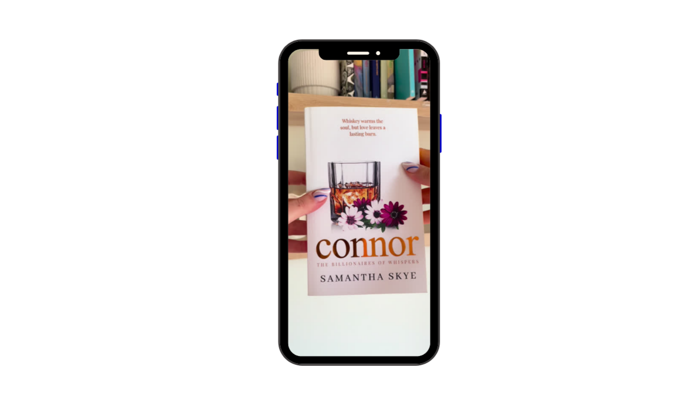 A person holding a book titled 'Connor' by Samantha Skye. The book cover features a glass of whiskey and some flowers, with a quote about whiskey at the top.