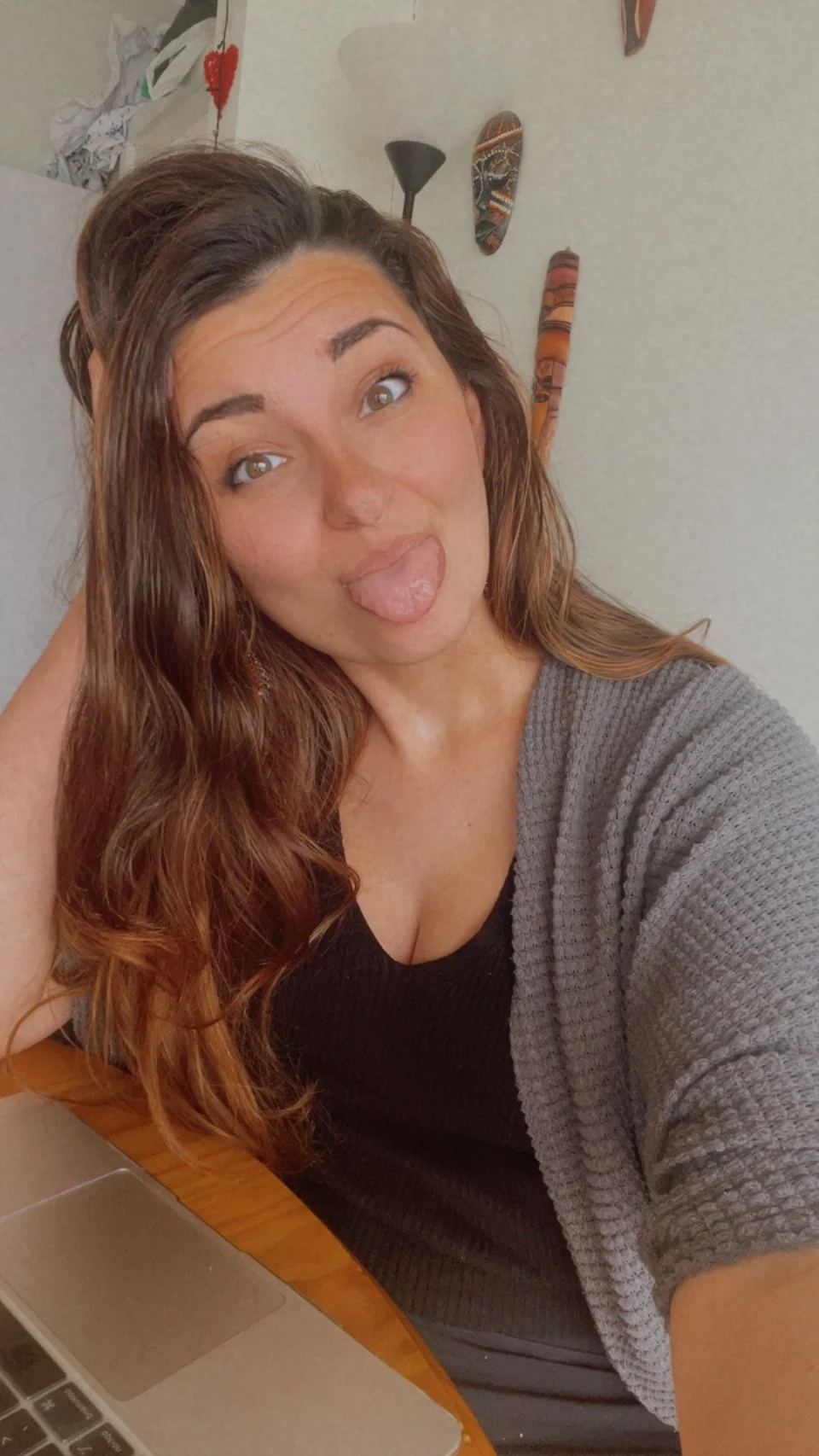 Sara, owner of Ancona Creative social media services for romance author. She has long brown hair making a silly face by sticking out her tongue, sitting at a table with a laptop in front of her.