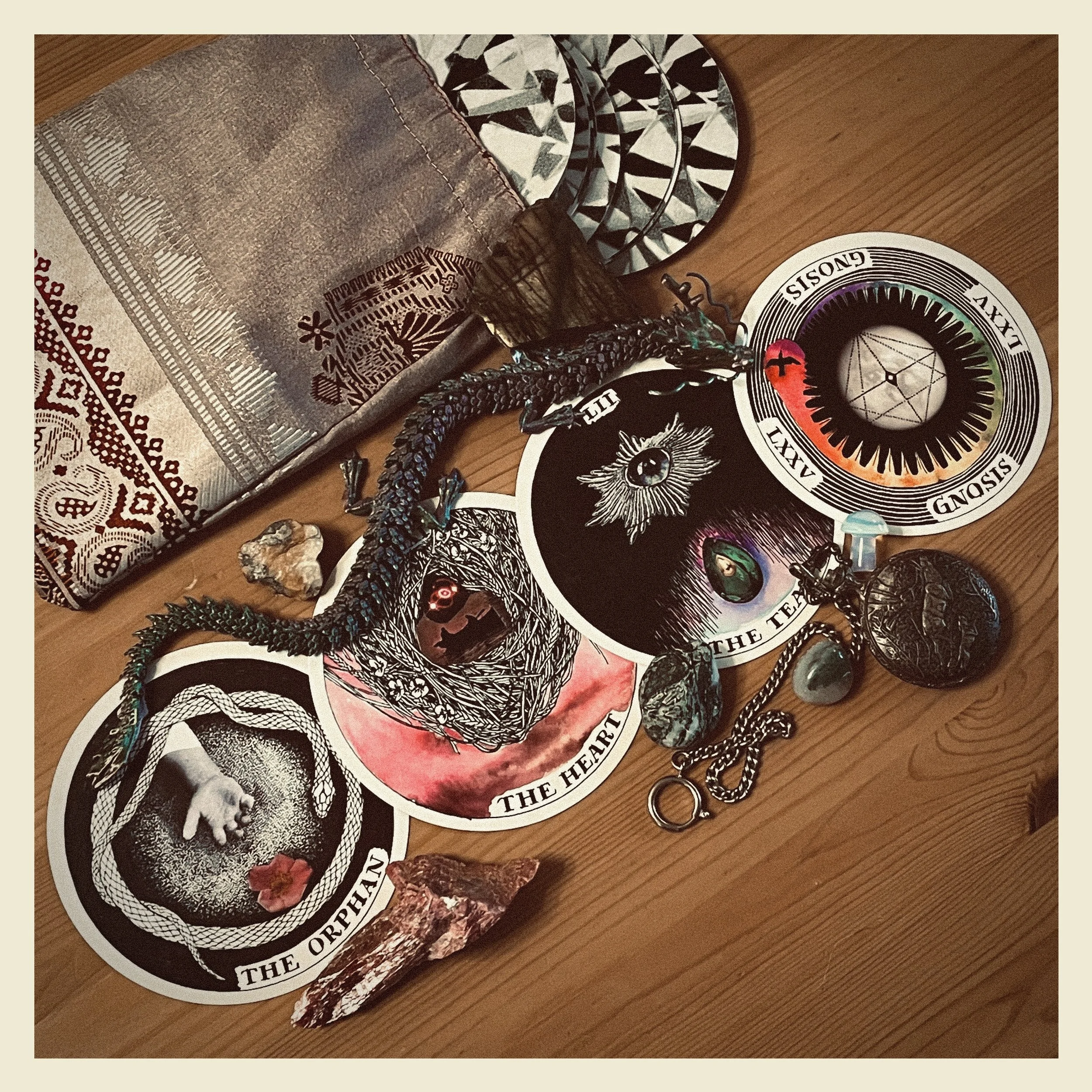 A collection of tarot cards, crystals, and jewelry on a wooden surface with a cloth and patterned items.