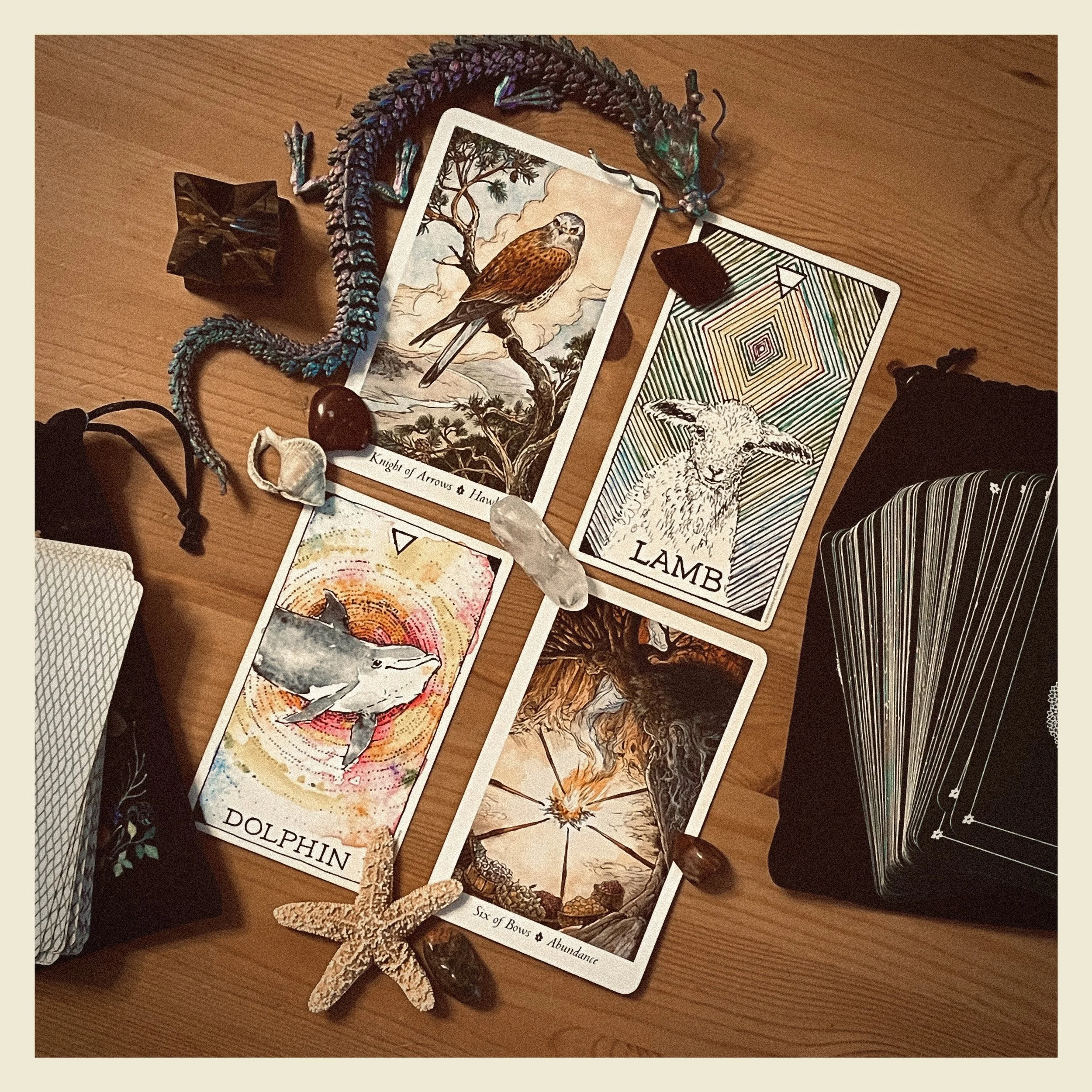 A wooden table with a collection of tarot cards featuring animals and nature themes, a beaded sculpture, and various small objects.