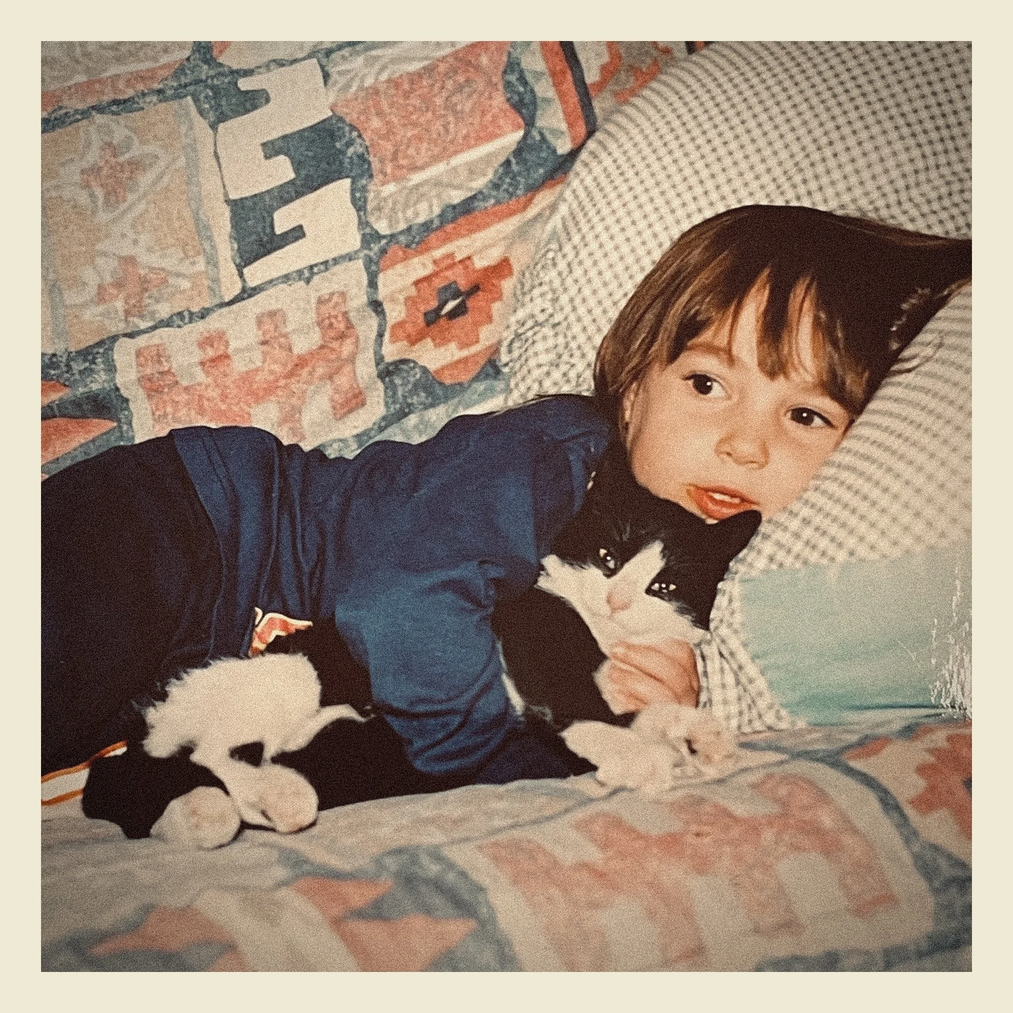 Partial view of a young child with brown hair and bangs lying on patterned bedsheets with a colorful quilt in the background.