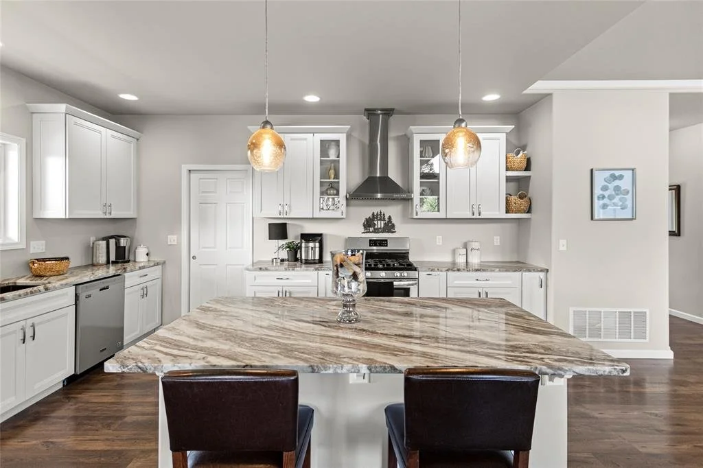 Modern kitchen with white cabinets, a large marble island, stainless steel appliances, and pendant lighting.