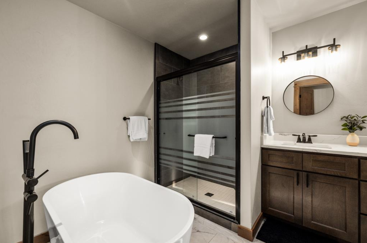 Modern bathroom with a white bathtub, a glass-enclosed shower, and a wooden vanity with a mirror and plant.