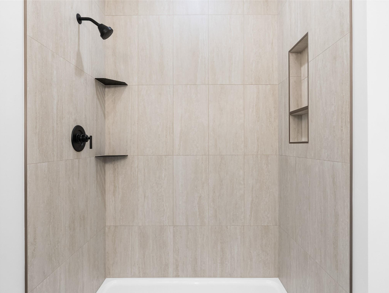 Empty walk-in shower with beige tiled walls, black fixtures, and built-in niche shelves.