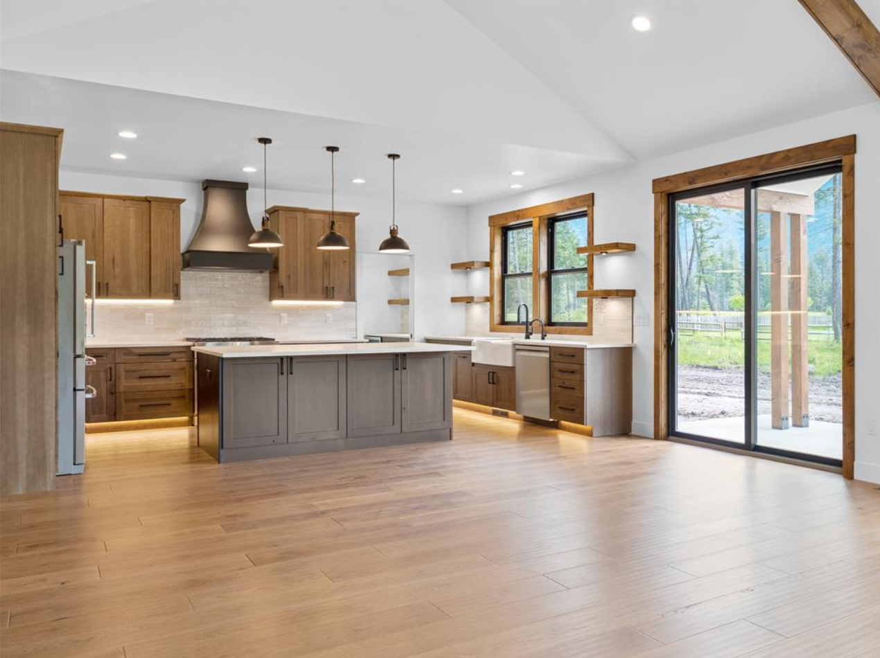 Modern kitchen with wooden cabinets, a gray kitchen island, and large windows overlooking an outdoor yard with trees.