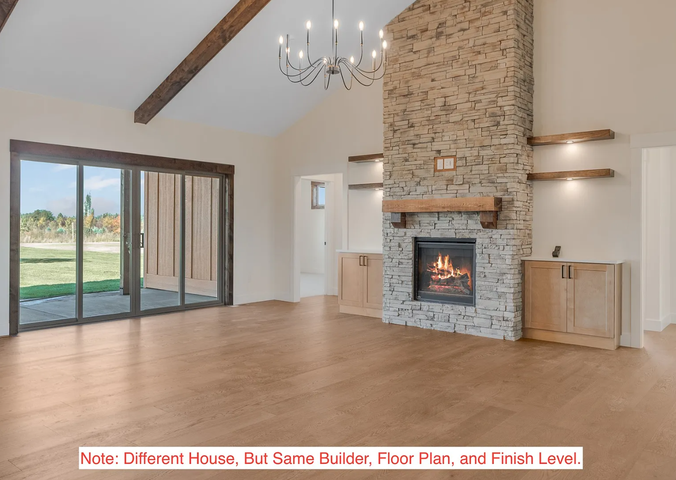 Living room with large glass sliding doors opening to an outdoor area, a stone fireplace with a wooden mantel, built-in cabinets on both sides, a chandelier hanging from a vaulted ceiling with exposed wooden beams, and hardwood flooring.