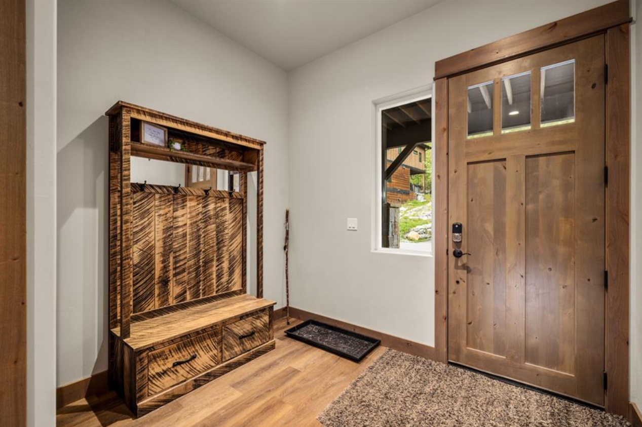 Entryway with a wooden front door, a small window, a wooden bench with a back, a coat rack, and a doormat on hardwood floor.