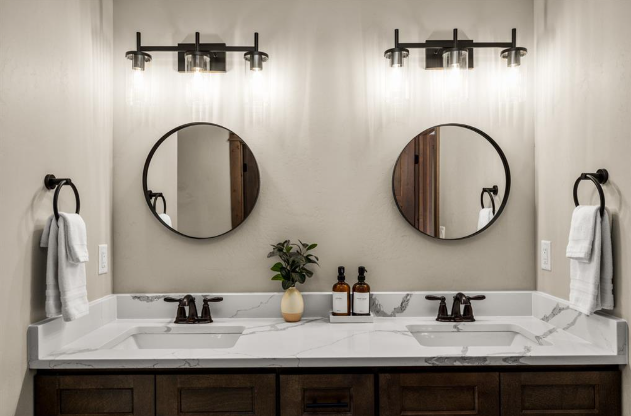 Double bathroom vanity with marble countertops, two sinks, round mirrors, black light fixtures, and white towels hanging on black towel rings.