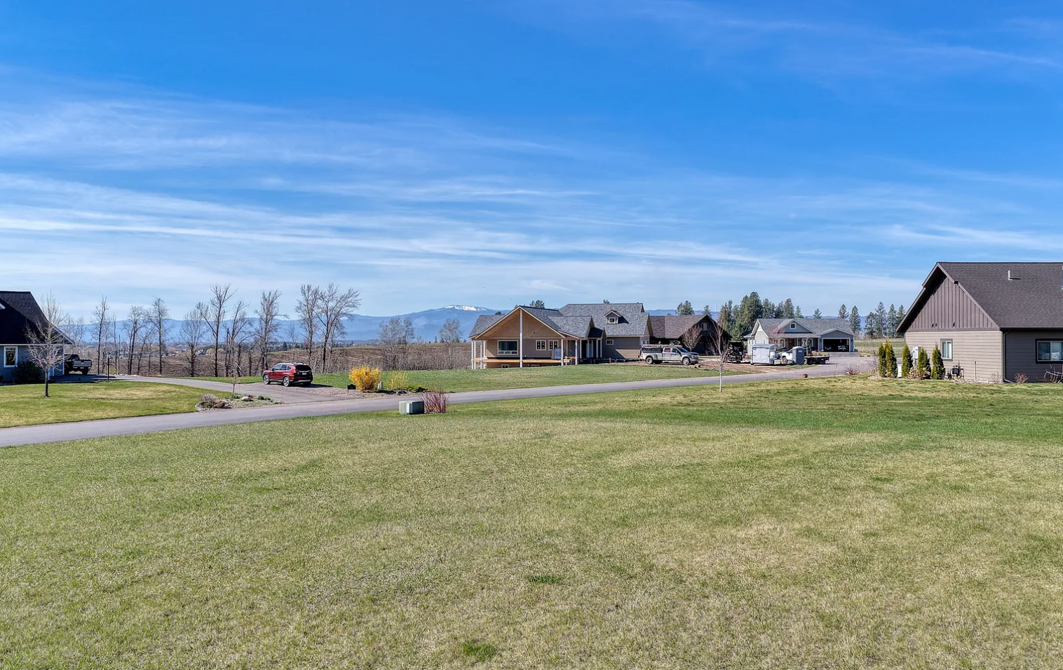 Suburban neighborhood with single-family homes, green lawns, a driveway, and distant mountains under a partly cloudy sky.