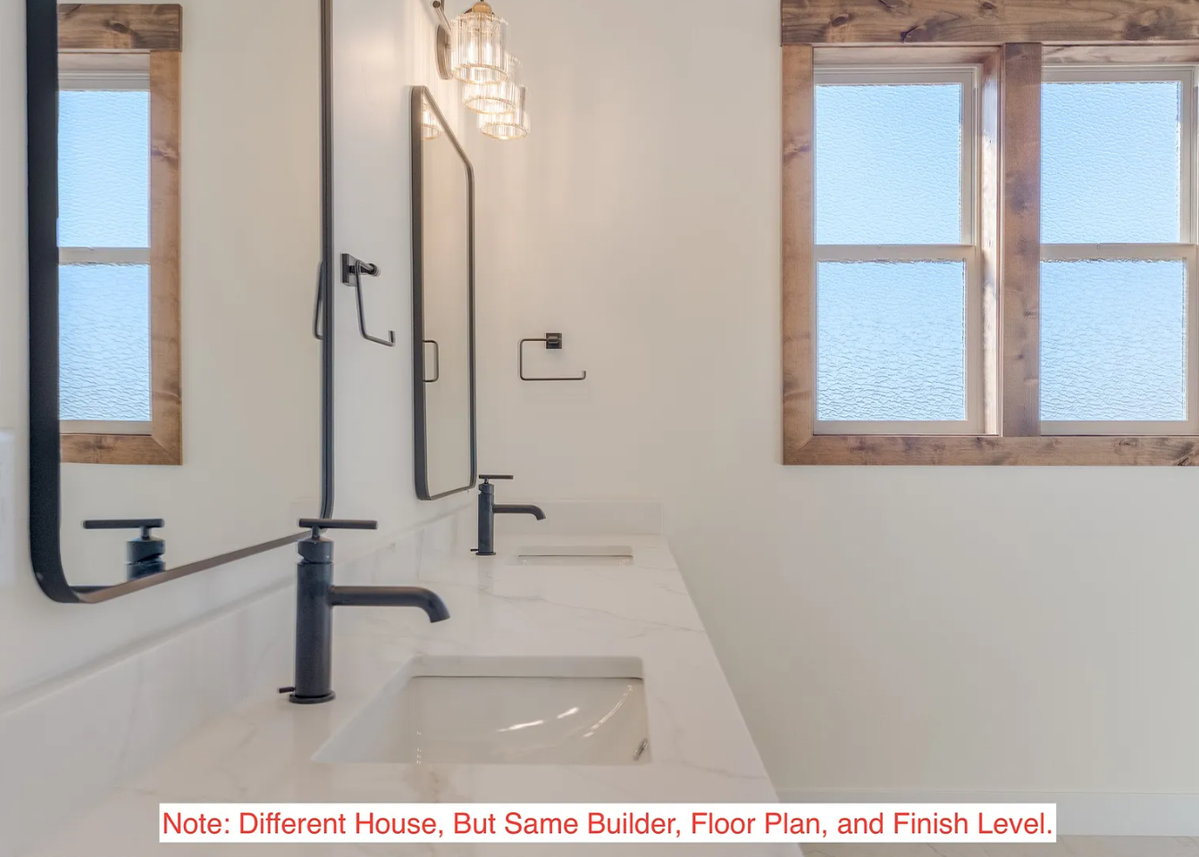 A modern bathroom with two windows, wooden trim, and a white countertop with two sinks and black faucets.