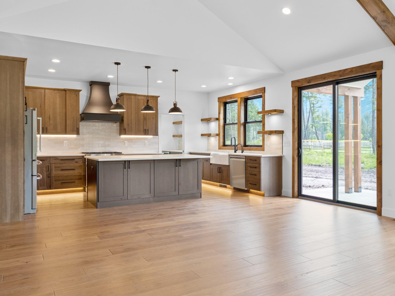 Modern kitchen with wooden cabinets, a large island, pendant lights, a sliding glass door, and windows overlooking greenery.