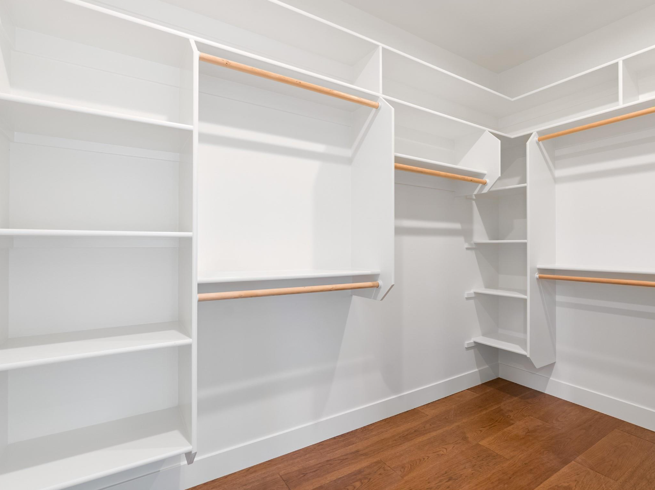 Empty white walk-in closet with built-in shelves and hanging rods, hardwood floor.