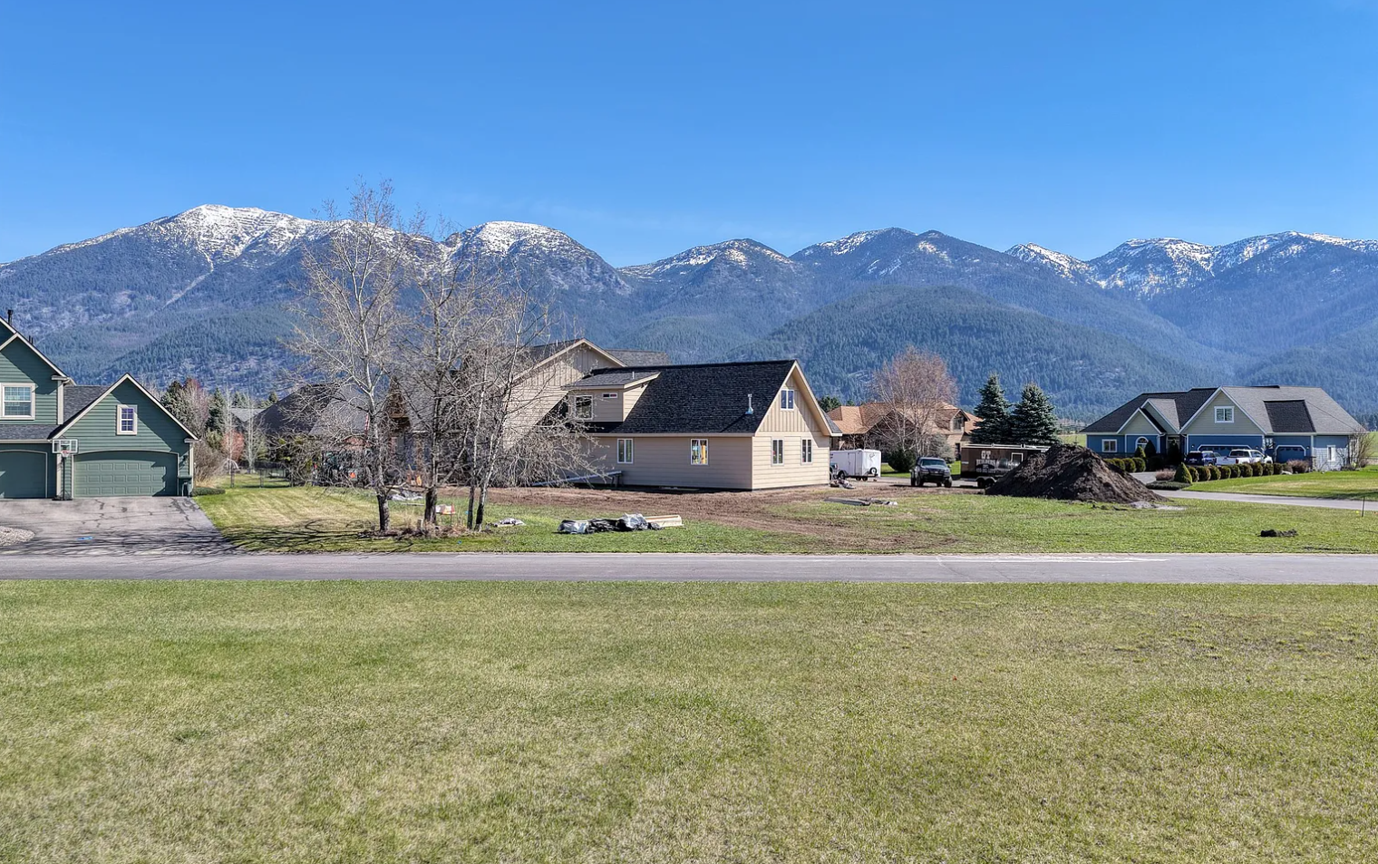 Suburban neighborhood with houses, a few trees, and a mountain range with snow in the background under a clear blue sky.