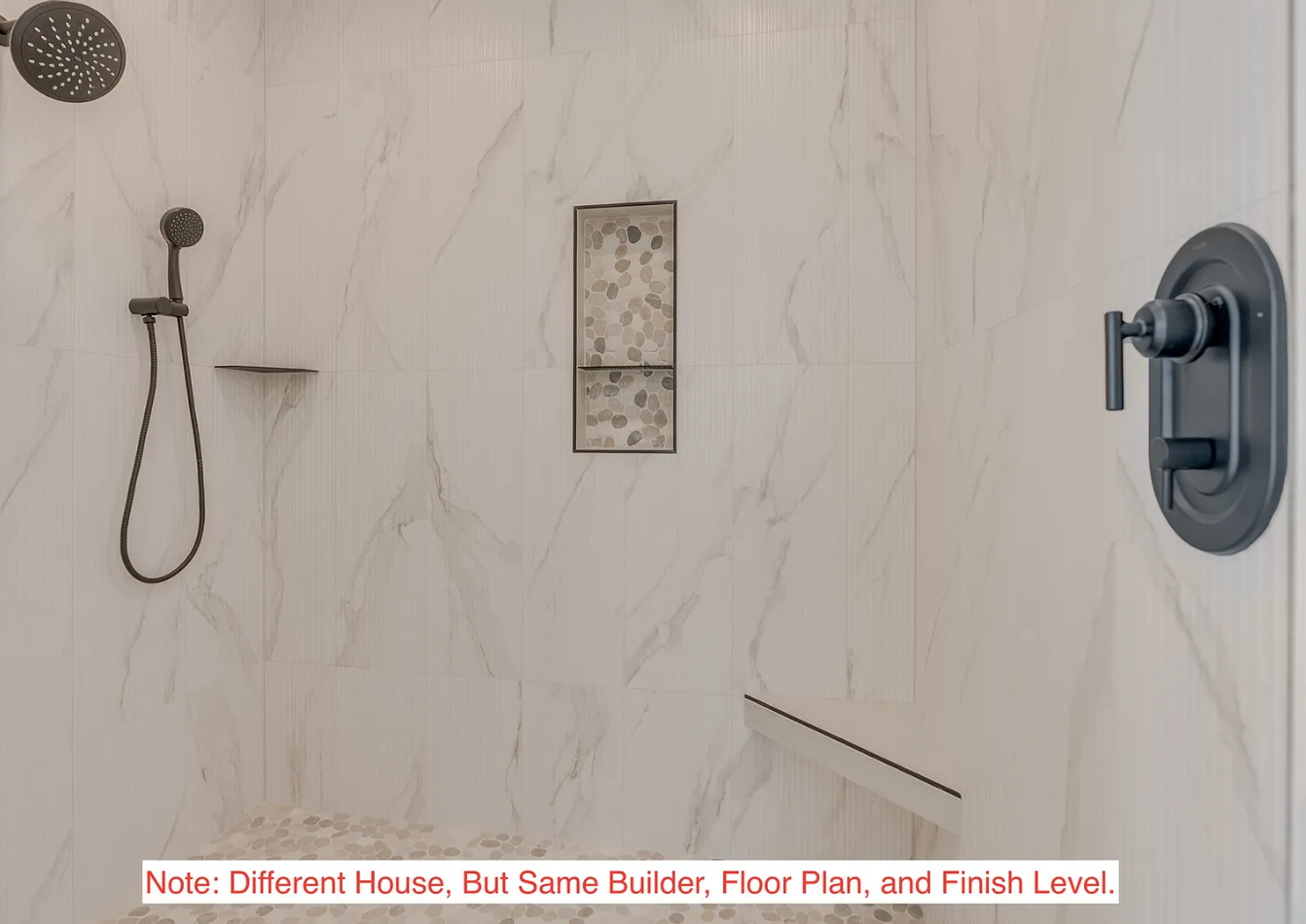 Interior of a modern walk-in shower with a handheld showerhead mounted on the wall, a built-in niche with pebble tile backing, and beige marble-like tiles on the walls.