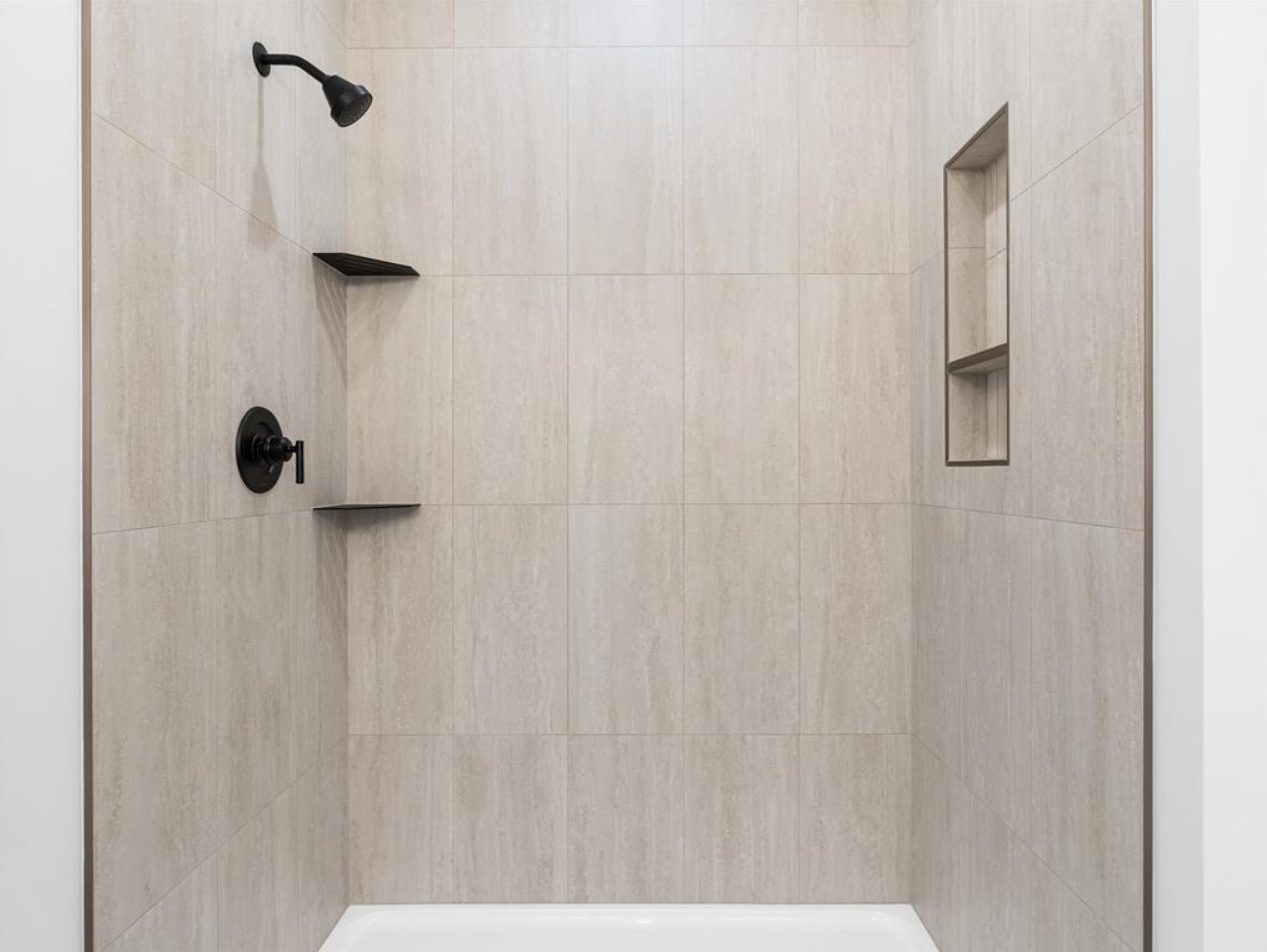 Empty walk-in shower with beige tiled walls, black showerhead, black control handle, built-in wall niches, and white shower base.