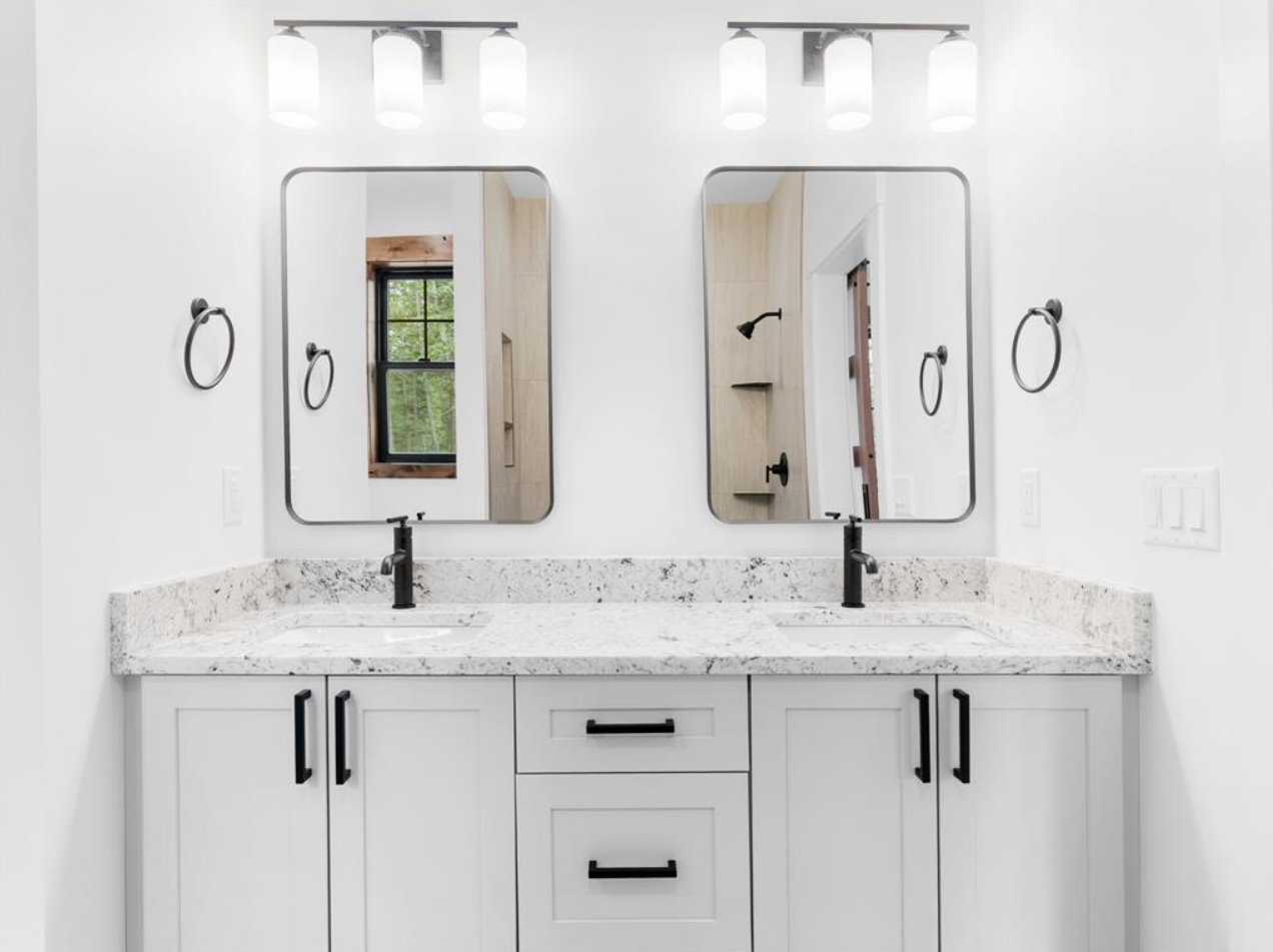 Bathroom with double vanity, white cabinets, granite countertop, two black faucets, two mirrors, and four ceiling lights.