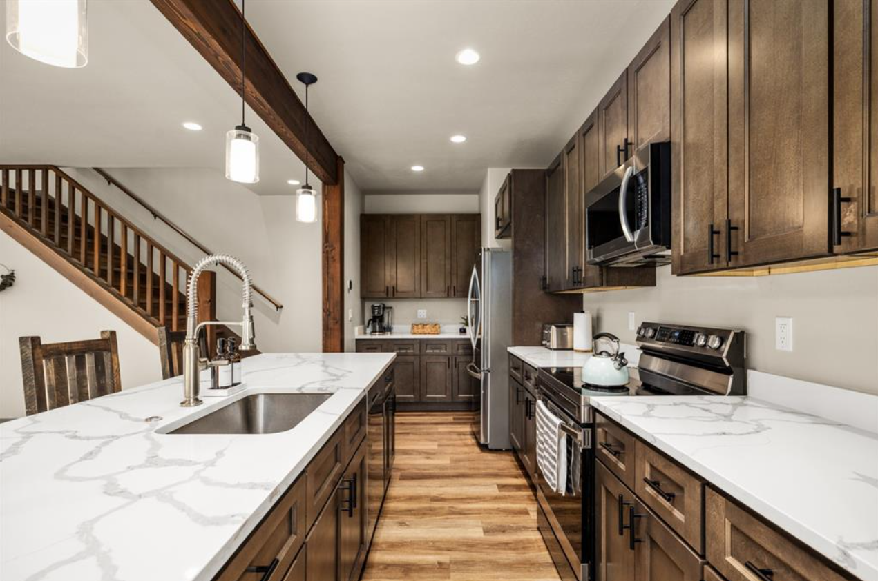 Modern kitchen with wooden cabinets, white marble countertops, stainless steel appliances, and hardwood flooring.