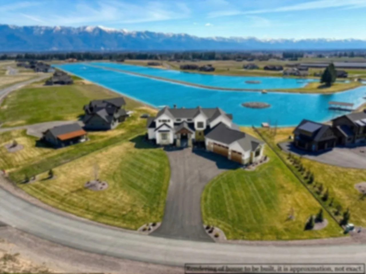 Aerial view of a suburban neighborhood near a large pond or lake with mountains in the background, several houses, well-maintained lawns, and a clear blue sky.