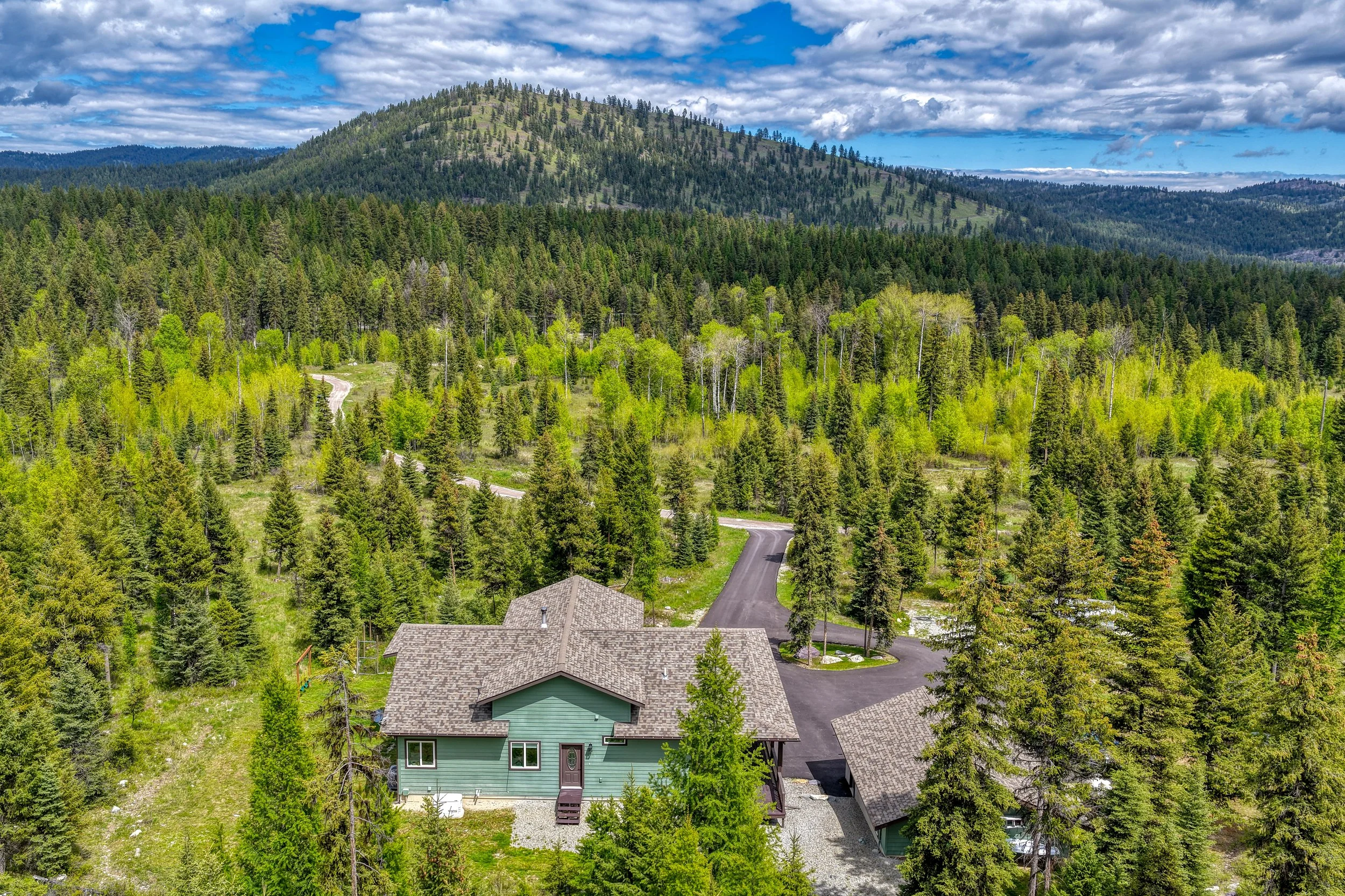 A house surrounded by trees with mountains in the background and a partly cloudy sky.
