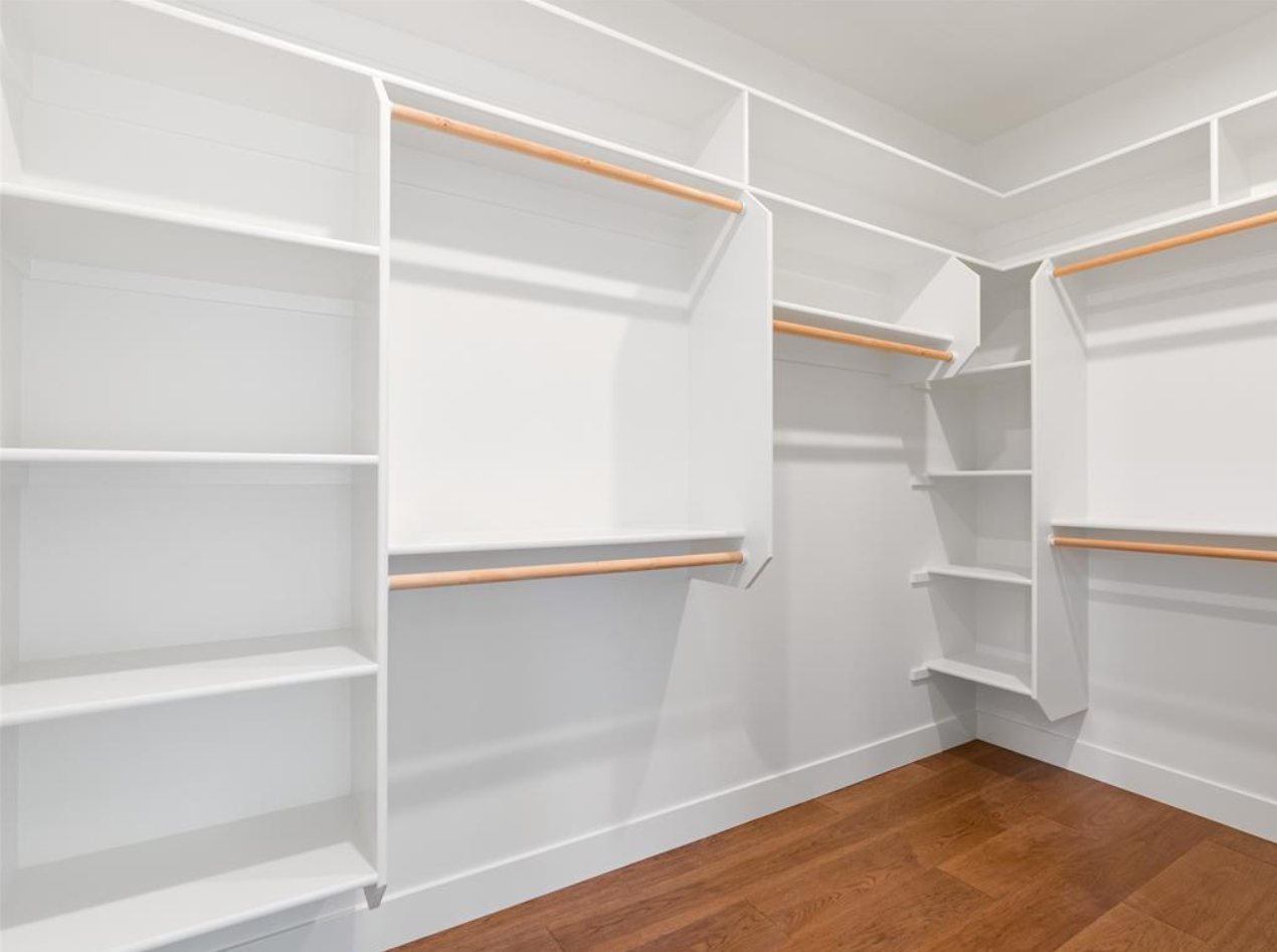Empty white walk-in closet with wooden shelves and hanging rods, and hardwood floor.