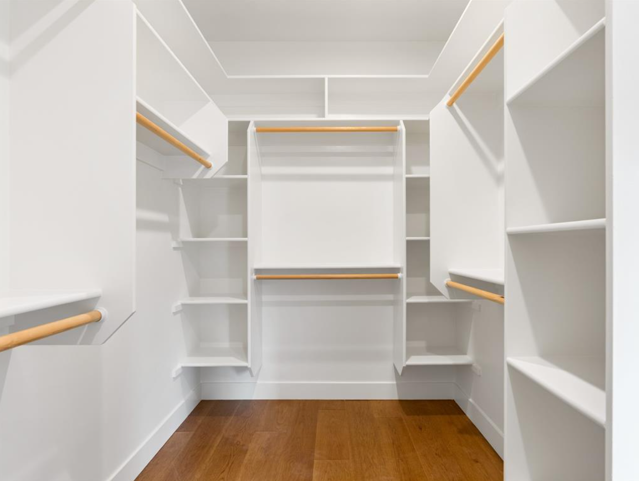 Empty white walk-in closet with built-in shelves and wooden hanging rods.