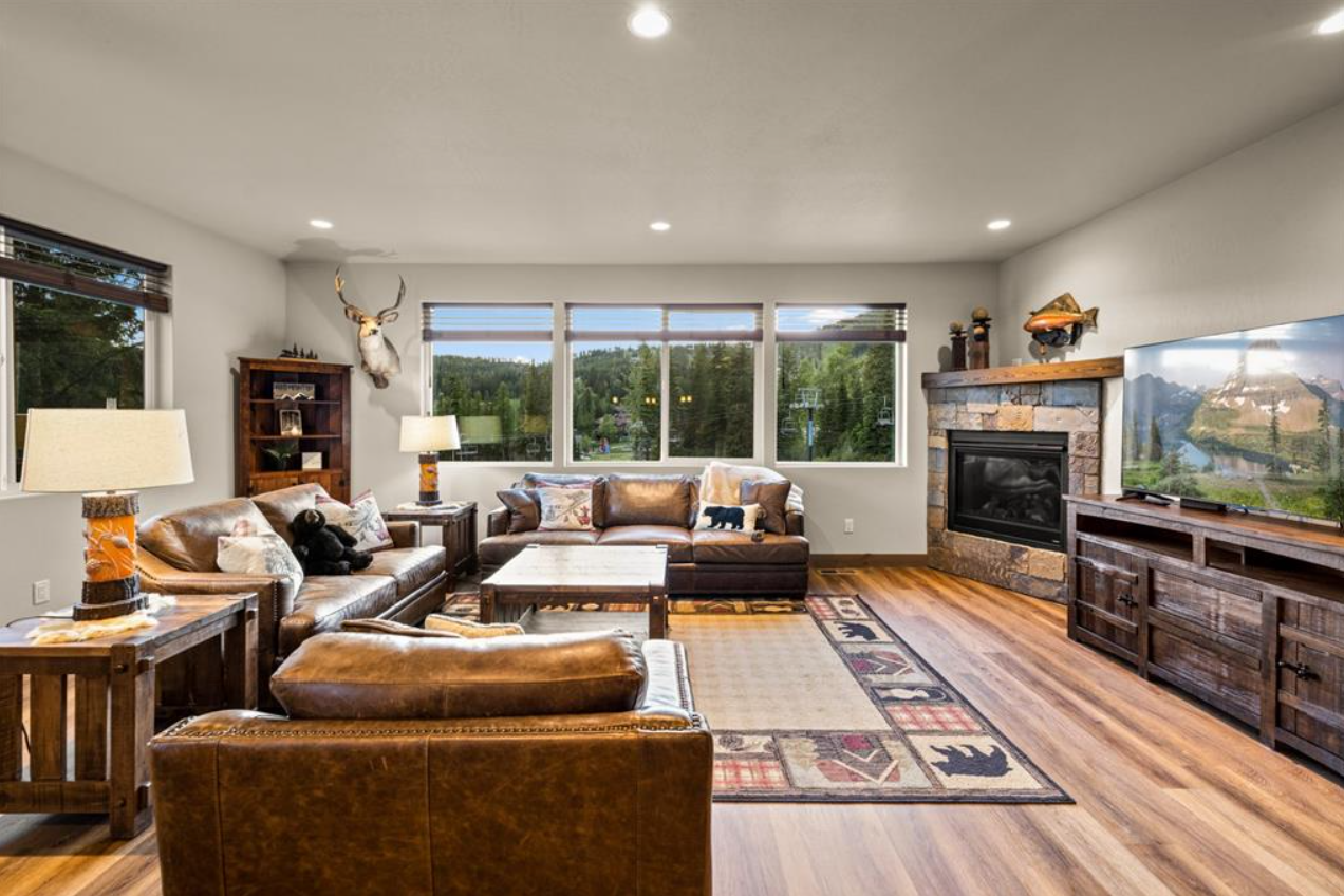 Living room with leather sofas, a wood fireplace, a large TV, wooden furniture, and a window view of trees and mountains.